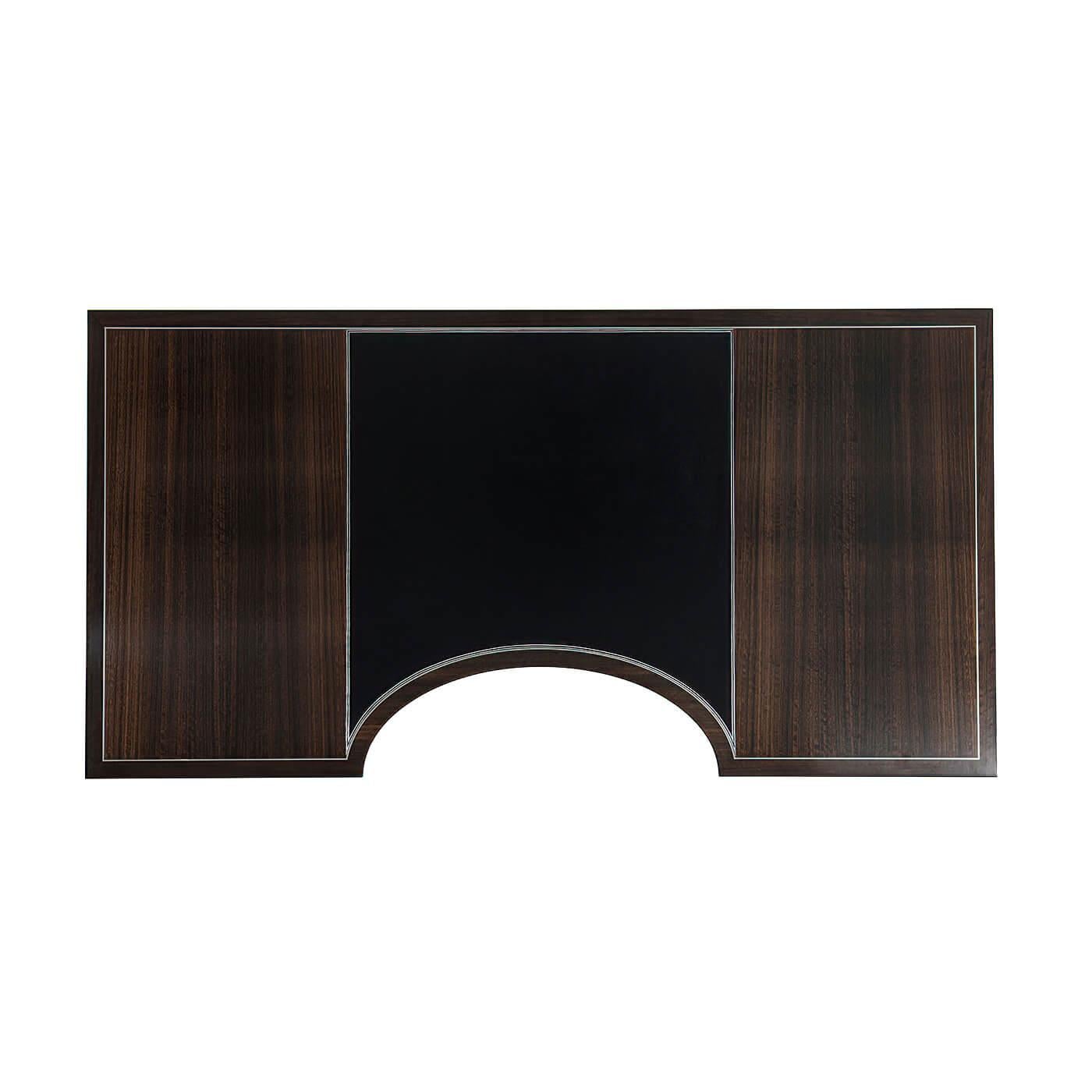 A French Art Deco style fumed figured Eucalyptus veneered desk, the rectangular stainless steel strung top centered by a tooled leather writing surface and a demi lune cut-out, with three frieze drawers with stainless steel handles, on turned legs