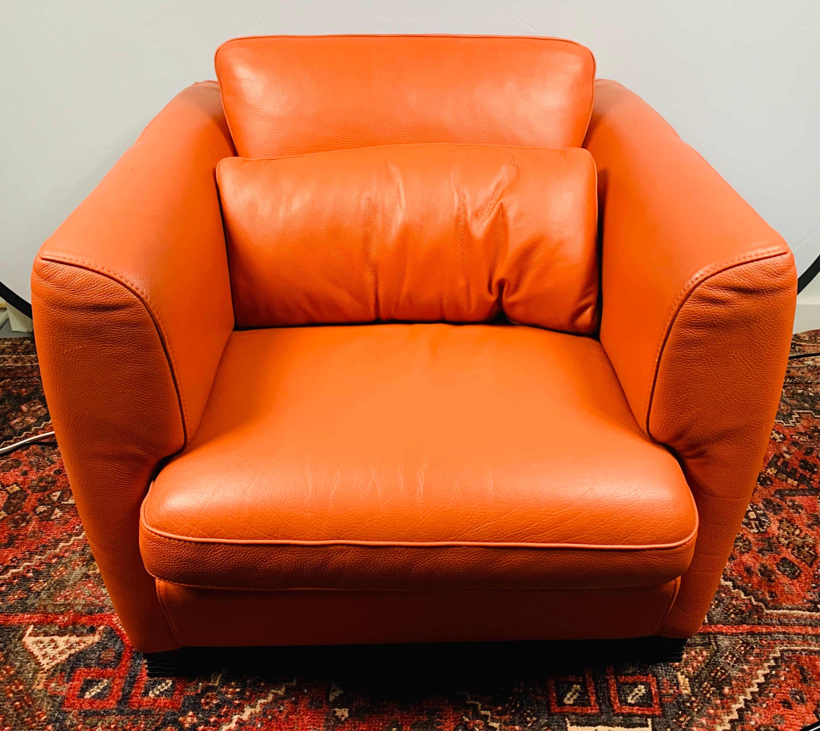 A timeless pair of Art Deco lounge chairs by Roche Bobois in a stunning fire orange. The chairs are finely upholstered in a soft leather with loose back and seat cushions over tightly upholstered box-form chair on stepped square feet. Comfortable