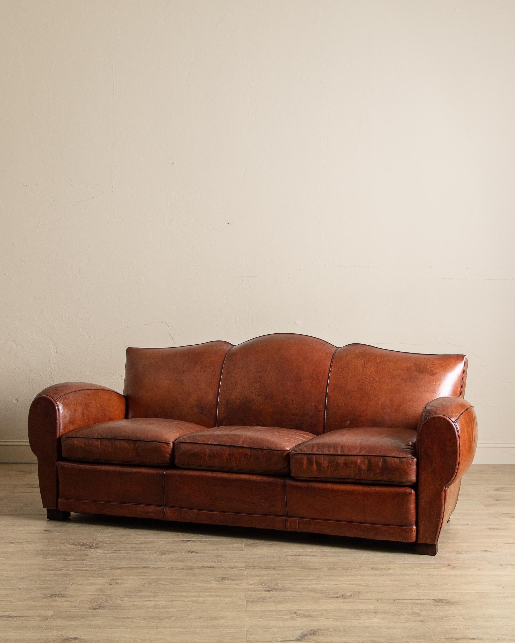 Questo divano club in pelle francese degli anni '30 è un esempio straordinario di design e artigianato senza tempo. Rivestito in ricca pelle cognac, il pezzo ha sviluppato una patina splendidamente usurata che ne esalta il calore, la profondità e