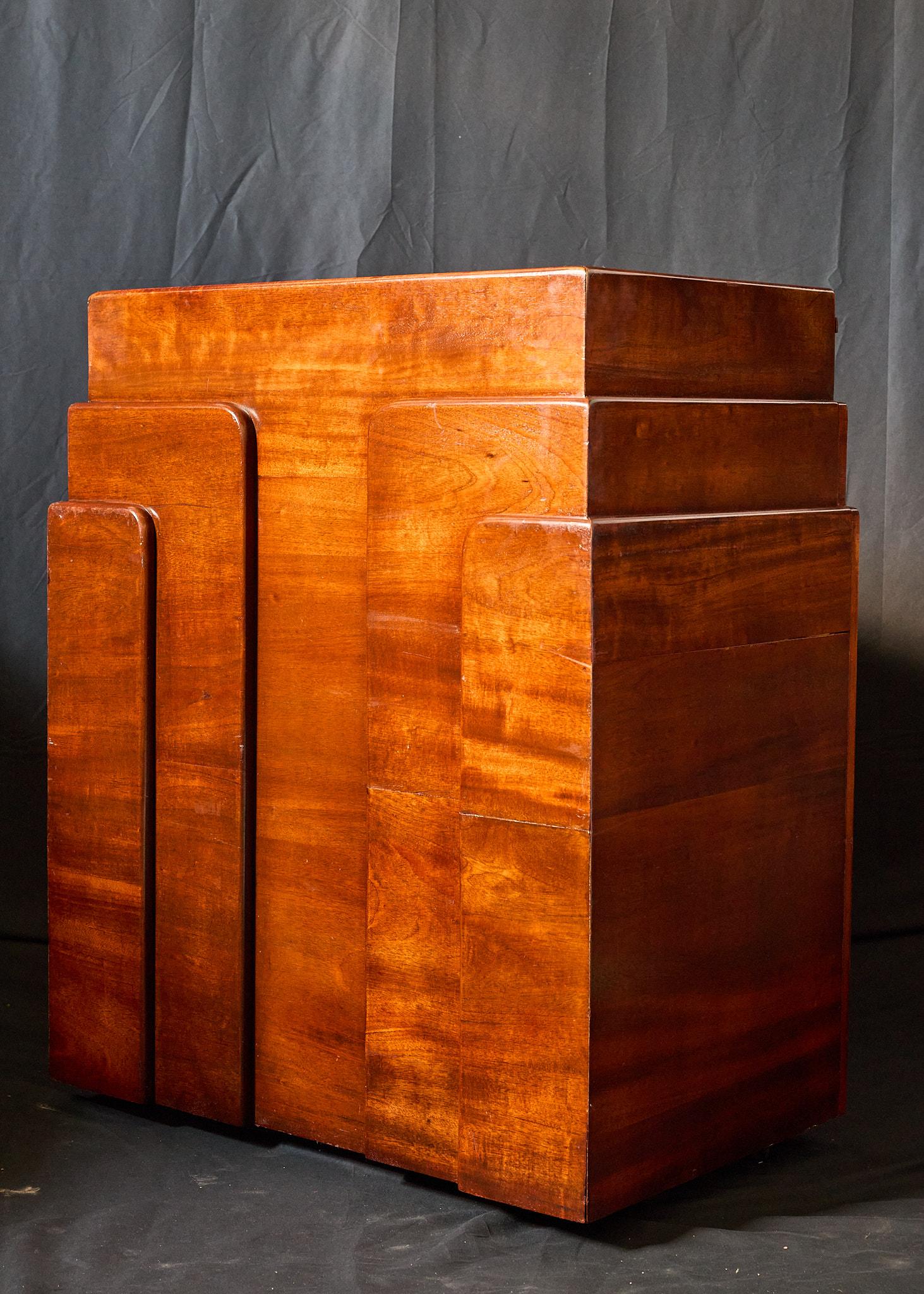 Art Deco lectern with classic sleek lines, iconic stepped design, and beautiful wood grain. The piece is made of mahogany with an inset flat and very slightly sloped work surface of black formica and a shelf for storage. There is an empty cavity
