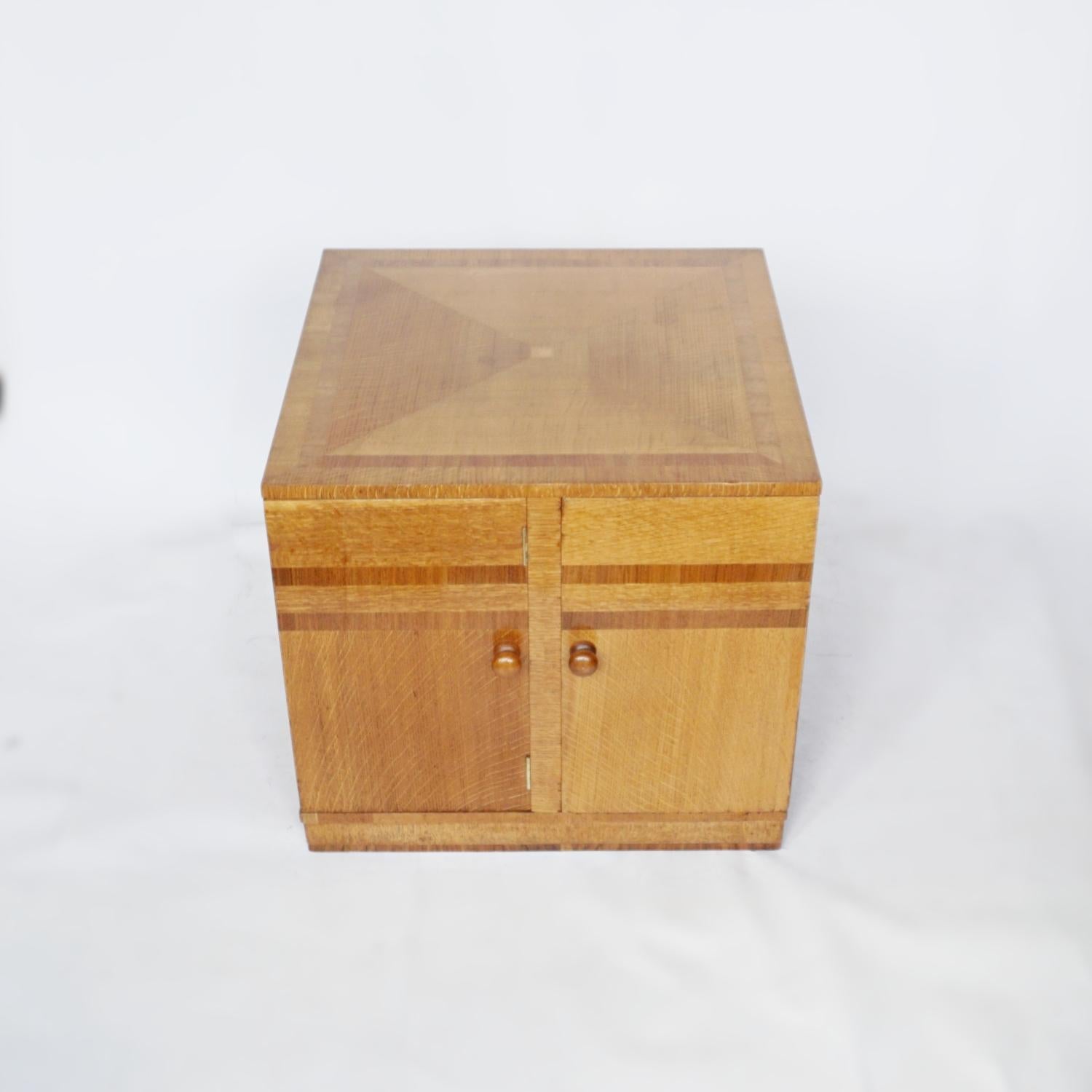An Art Deco library table. Square form library table consisting of two cupboard doors for storage or larger books, and two pull out book shelves/side tables. Oak veneered with figured walnut banding. Original wooden handles. 

Dimensions: H 56cm W