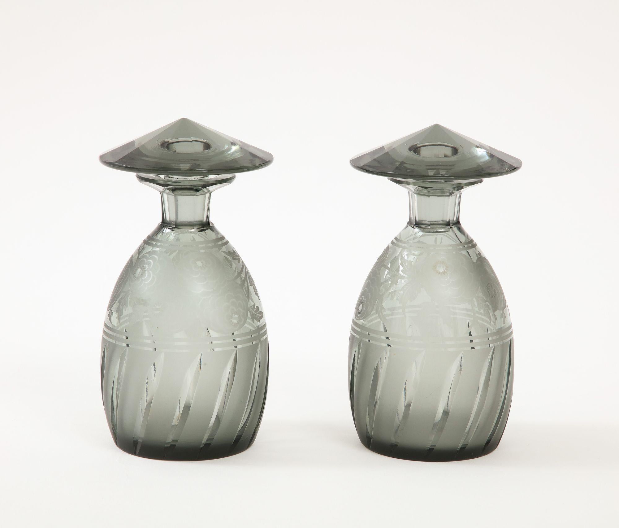 A pair of period Art Deco cut crystal lidded light lavender grey Art Deco lidded bottles. These fabulous bottles are ovoid forms with lozenge cut bases grey crystal with an etched floral deco design and topped with faceted conical stoppers. Signed