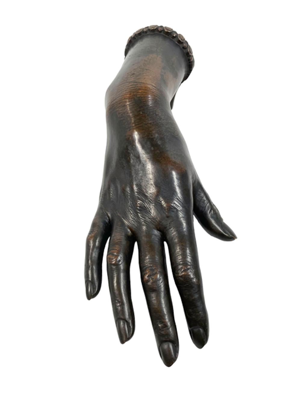 Life-size patinated cast bronze study of a ladies hand with a bracelet on her arched wrist which is raised on a support dated 1926.