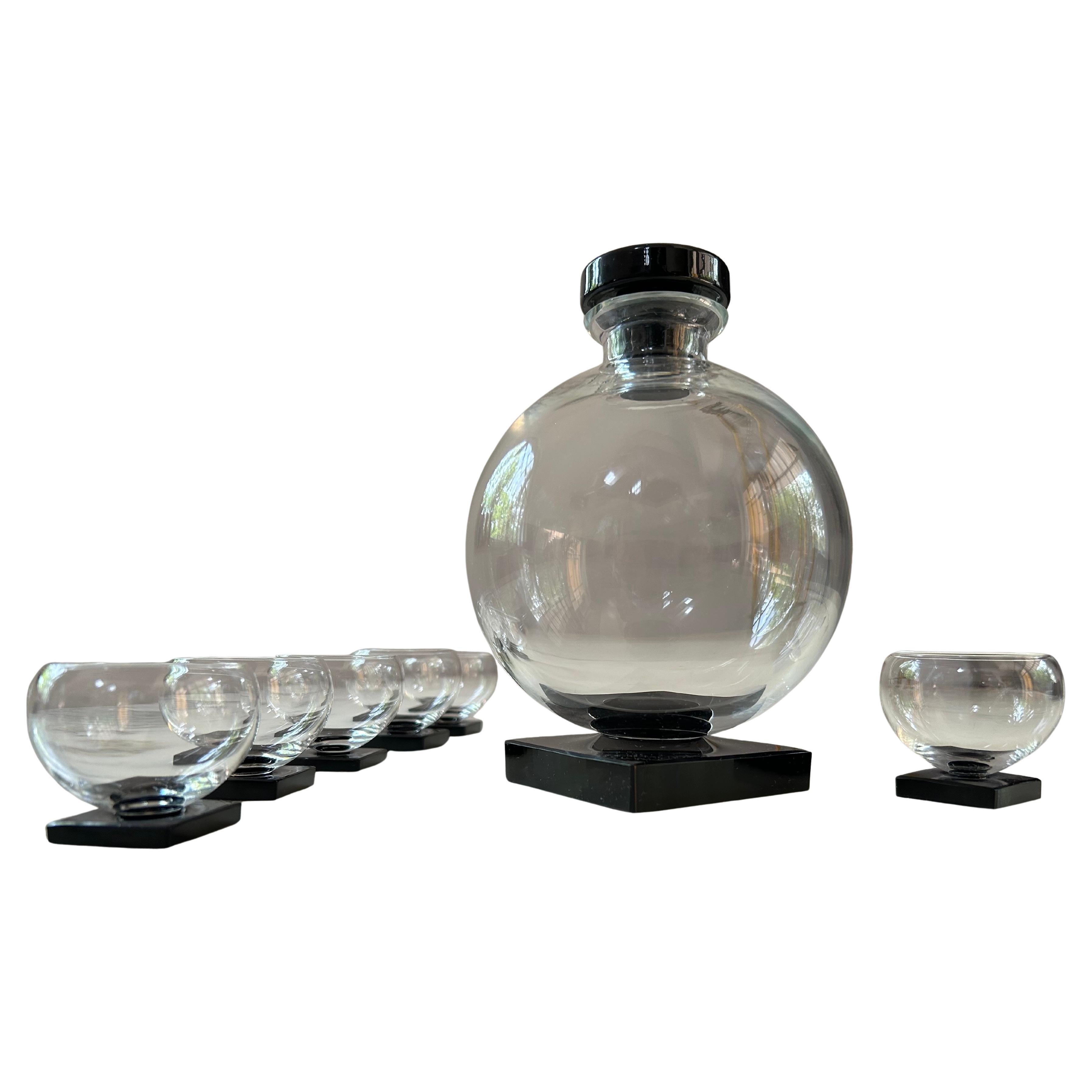 With bold, geometric shapes and streamlined, modern aesthetics, this Art Deco set is comprised of a clear glass ball decanter with its original Onyx stopper and six glasses, all on black Onyx bases.

Although no makers mark is visible, this ensemble