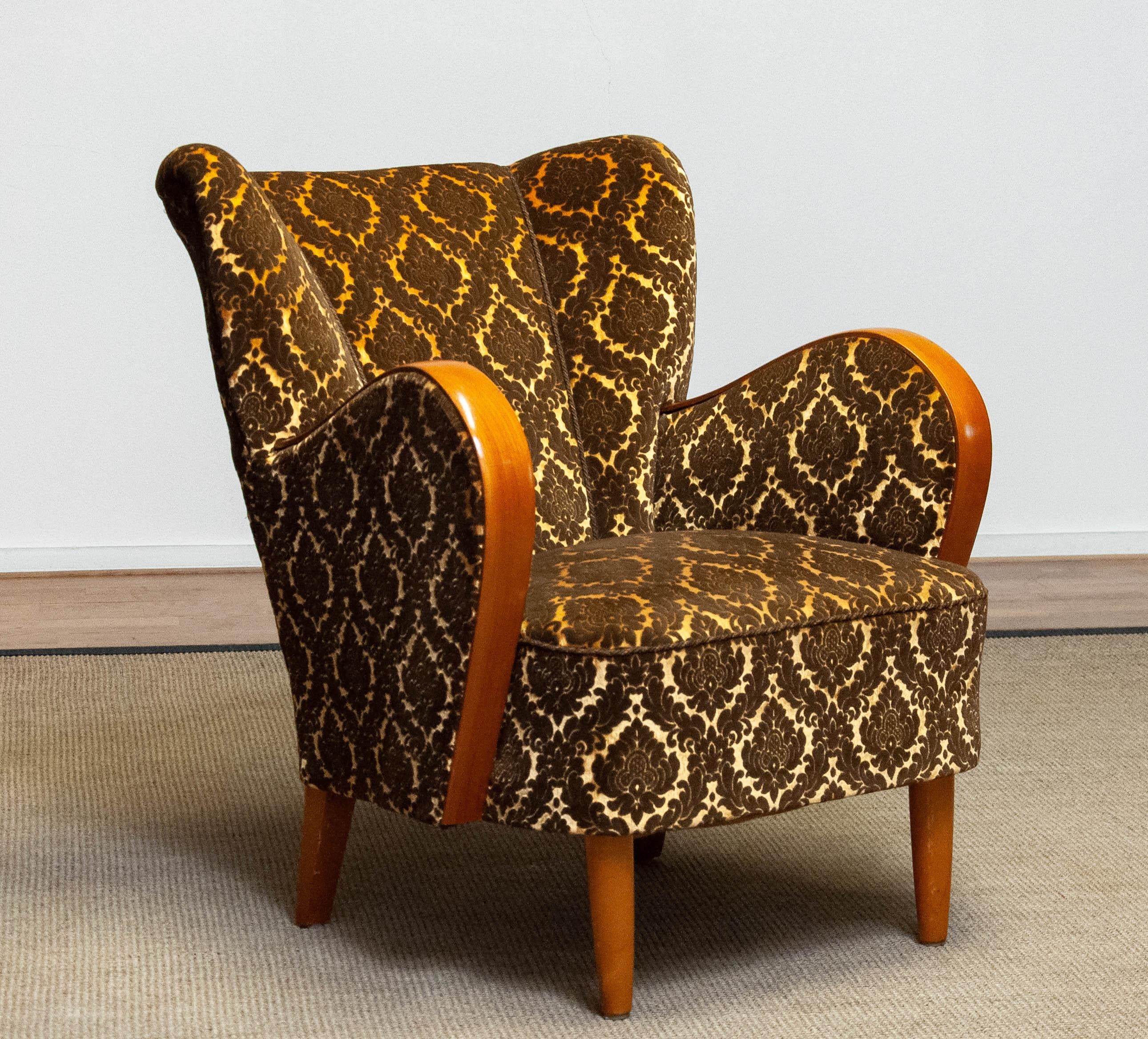 Absolut schöner und vollständiger originaler skandinavischer Lounge-/Clubsessel im Stil von Fritz Hansen aus Dänemark.
Dieser Lounge-/Clubsessel ist mit einem goldfarbenen und braunen Jacquard-Samtstoff gepolstert. Die Armlehnen aus Bugholz sind aus
