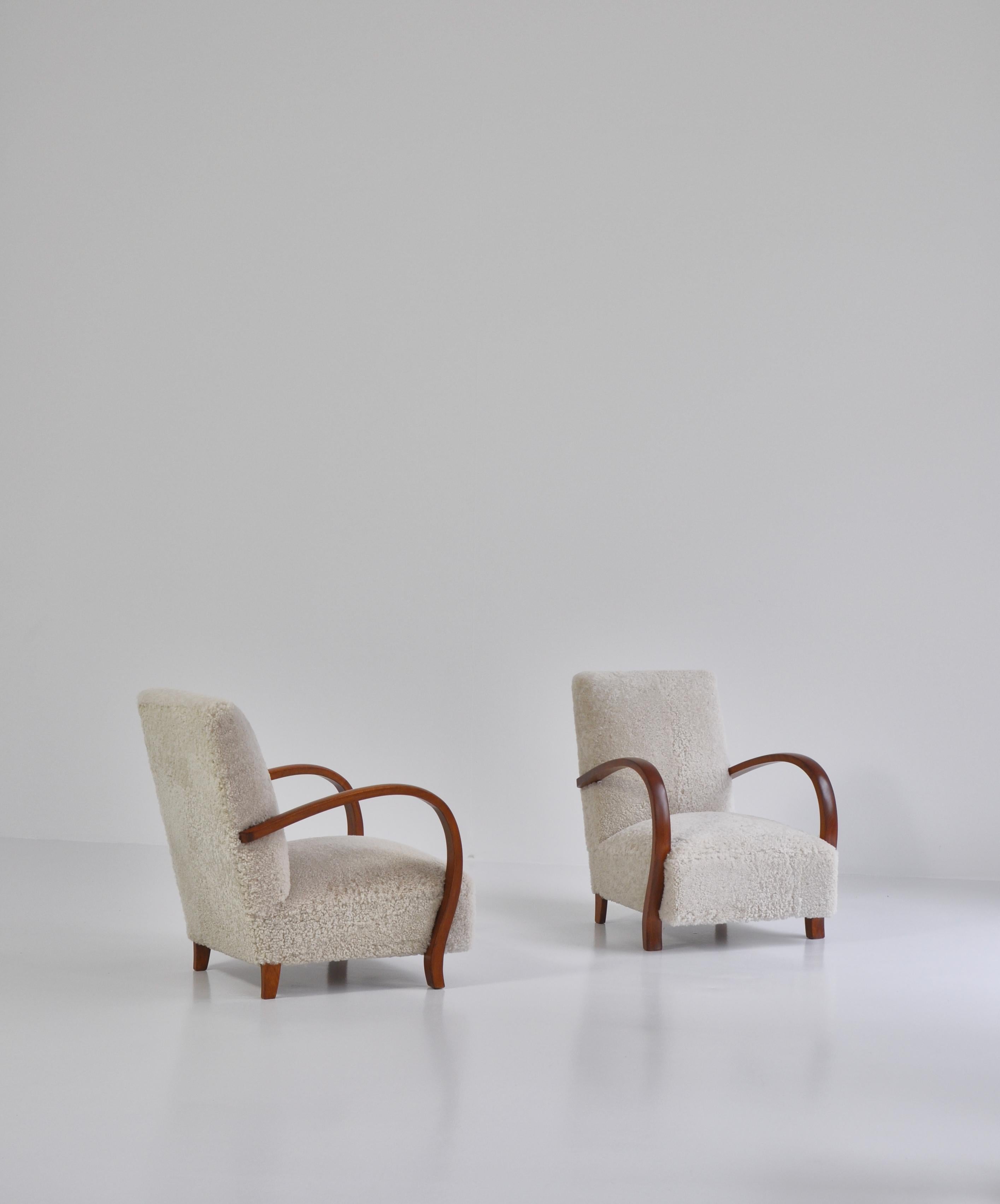 Stunning pair of lounge chairs made in the 1930s by a Danish cabinetmaker. Reupholstered in soft natural sheepskin. The chairs feature beautifully curved armrest in dark stained beech. In the style of Fritz Hansen.