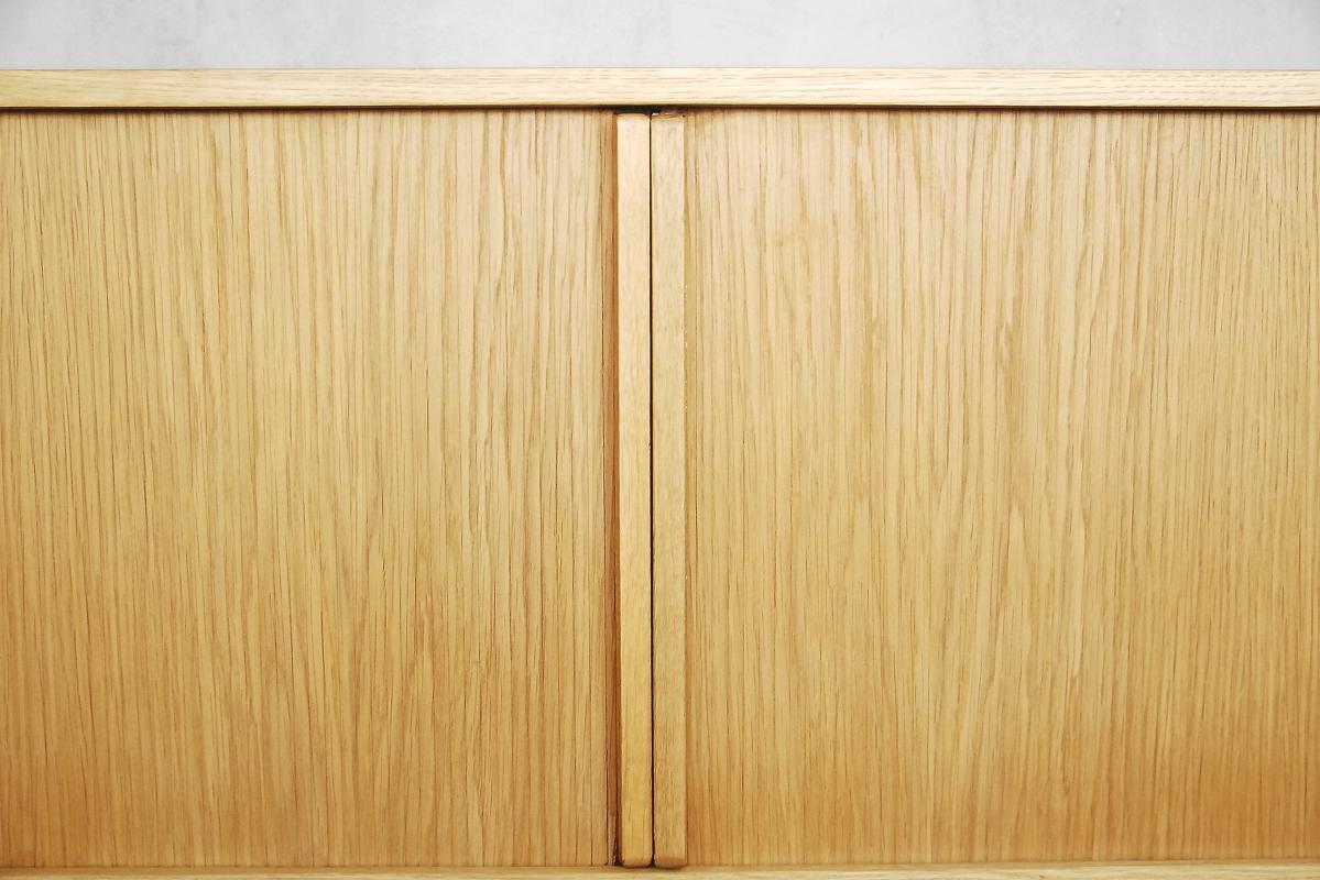 This Bauhaus style low cabinet sideboard was manufactured in Germany during the 1960s. It is made from oak wood and veneer with regular and beautiful grain. The piece features two hidden tambour sliding doors and shelves inside. The sideboard is