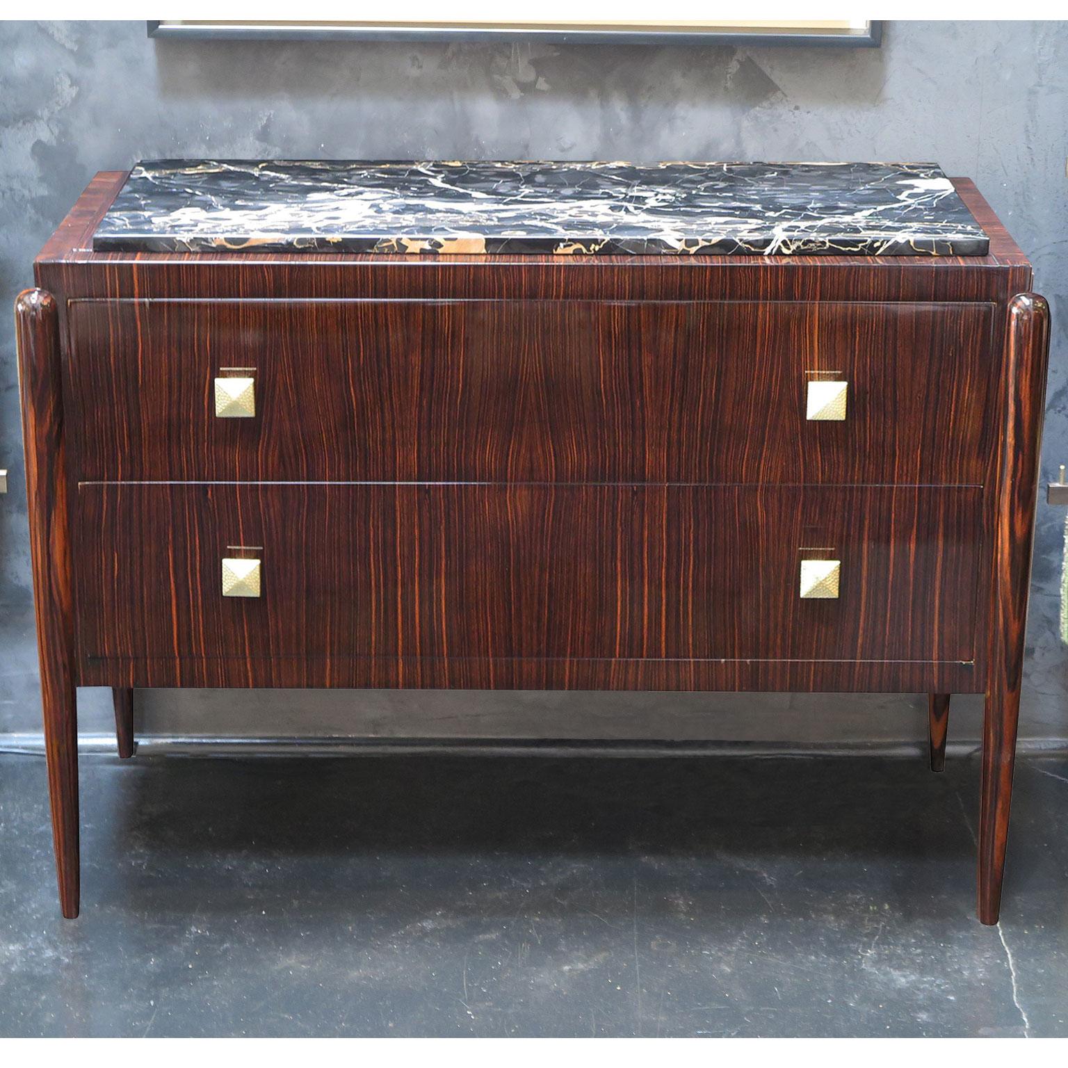 Art Deco dresser with Macassar ebony frame and rounded, tapered legs. Original marble top gives this commode an elegant look and allows for a durable surface. Two drawers, with hammered brass hardware, offer ample storage space . 
Dresser is in