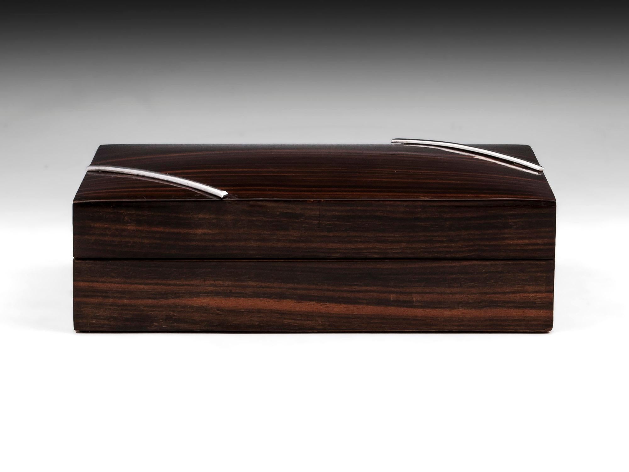 Art Deco jewelry box veneered in Macassar ebony with two silver plated half round bars angled on the top. The interior has an unusual cantilever insert with padded velvet compartments, with the box itself being lined in faux snakeskin leather.