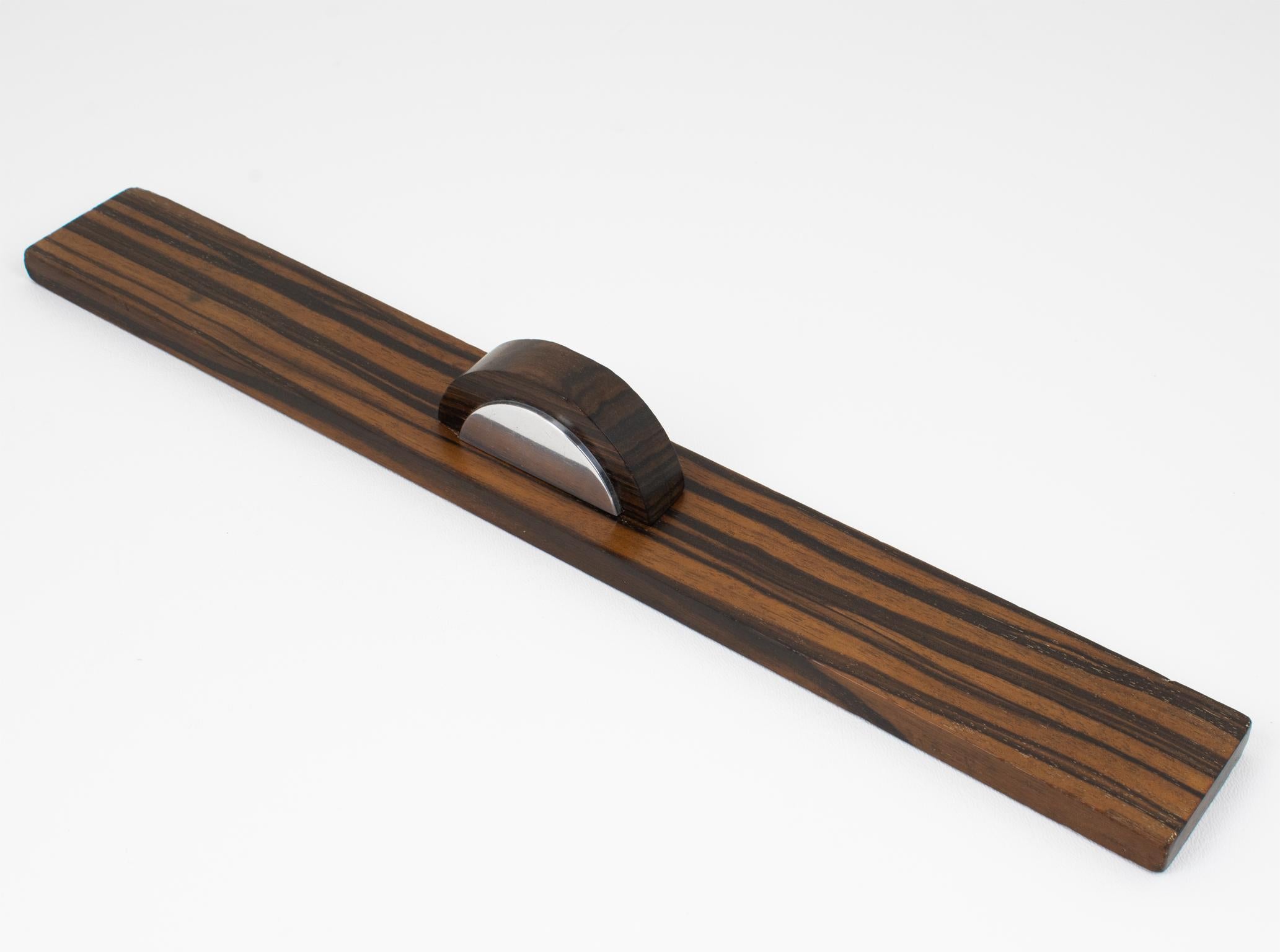Dieses schöne Art-Deco-Schreibtischset mit Lineal ist das perfekte Accessoire für jedes raffinierte Büroambiente. Das Lineal ist aus Makassar-Holz mit einem verchromten Metallakzent gefertigt. Die geometrische Form ist einfach, aber effizient und