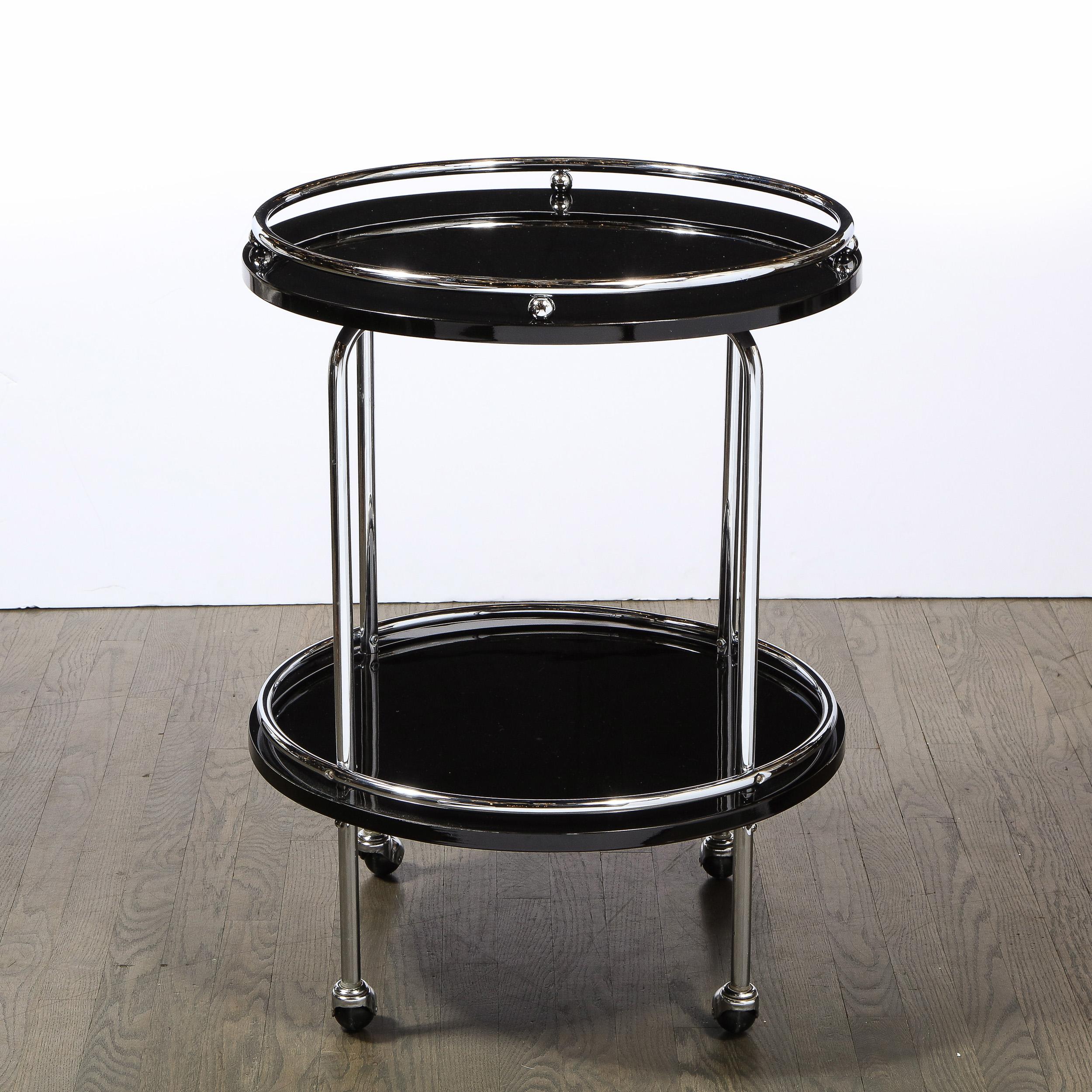 This stunning Art Deco Machine Age two tier bar/ serving cart was realized in the United States, circa 1935. Sitting on orbital castors, the piece features a polished chrome body consisting of four streamlined supports that connect two circular tops