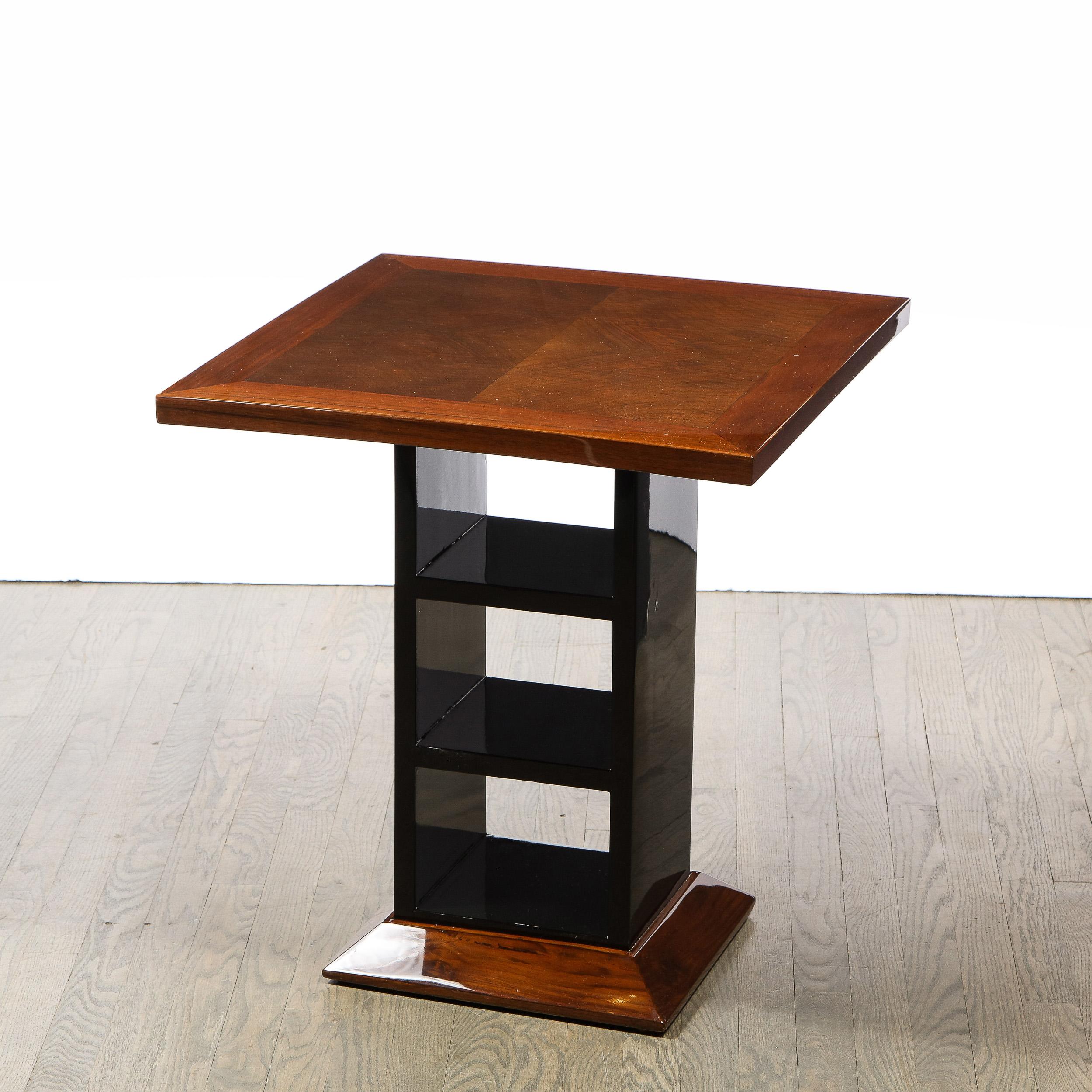 This stunning Art Deco Machine Age side/end table was realized in the United States circa 1935. It features a beveled base; an open form black lacquer body with two perpendicular supports; and a square top in bookmatched walnut. With its graphic