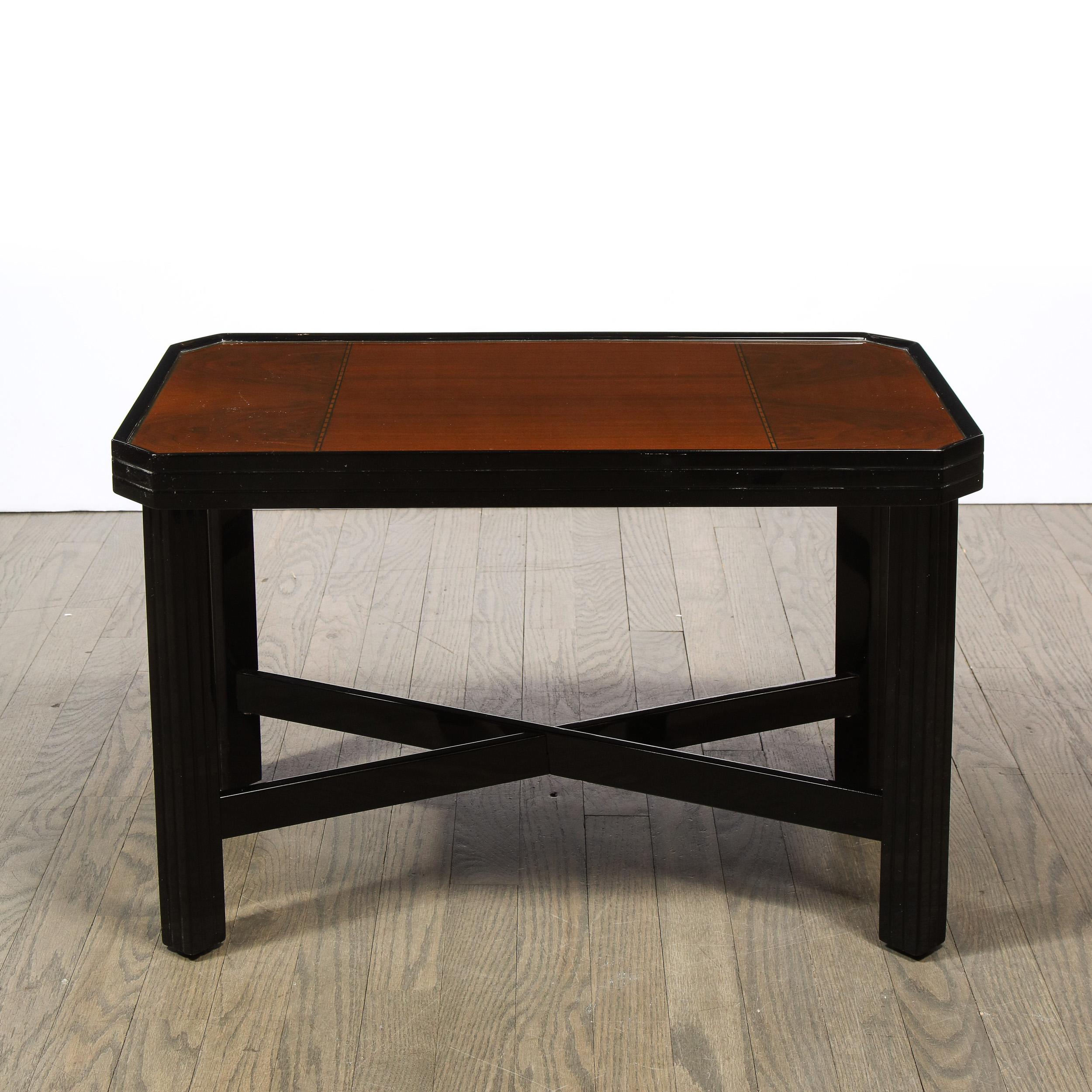 This elegant Art Deco Machine Age table was realized in the United States circa 1935. It features rectilinear legs connected by x form supports- all in lustrous black lacquer. The top features a bookmatched walnut center bookended on each side by