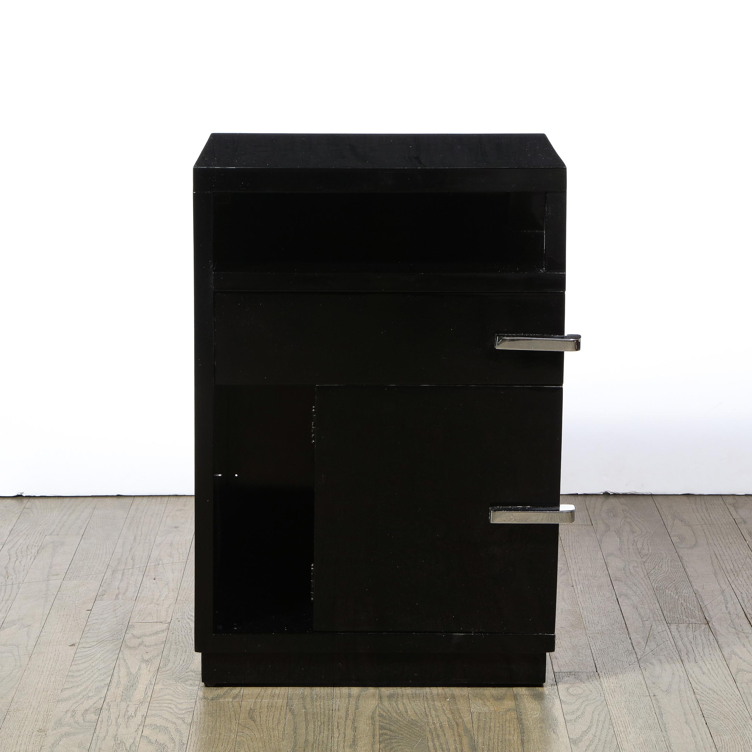 This Art Deco, Machine Age, smoothly finished black lacquer nightstand was created in the United States circa 1935. Volumetric rectangular body with open-cornered top shelf followed below by a pull-out drawer and hinged door provides ample storage