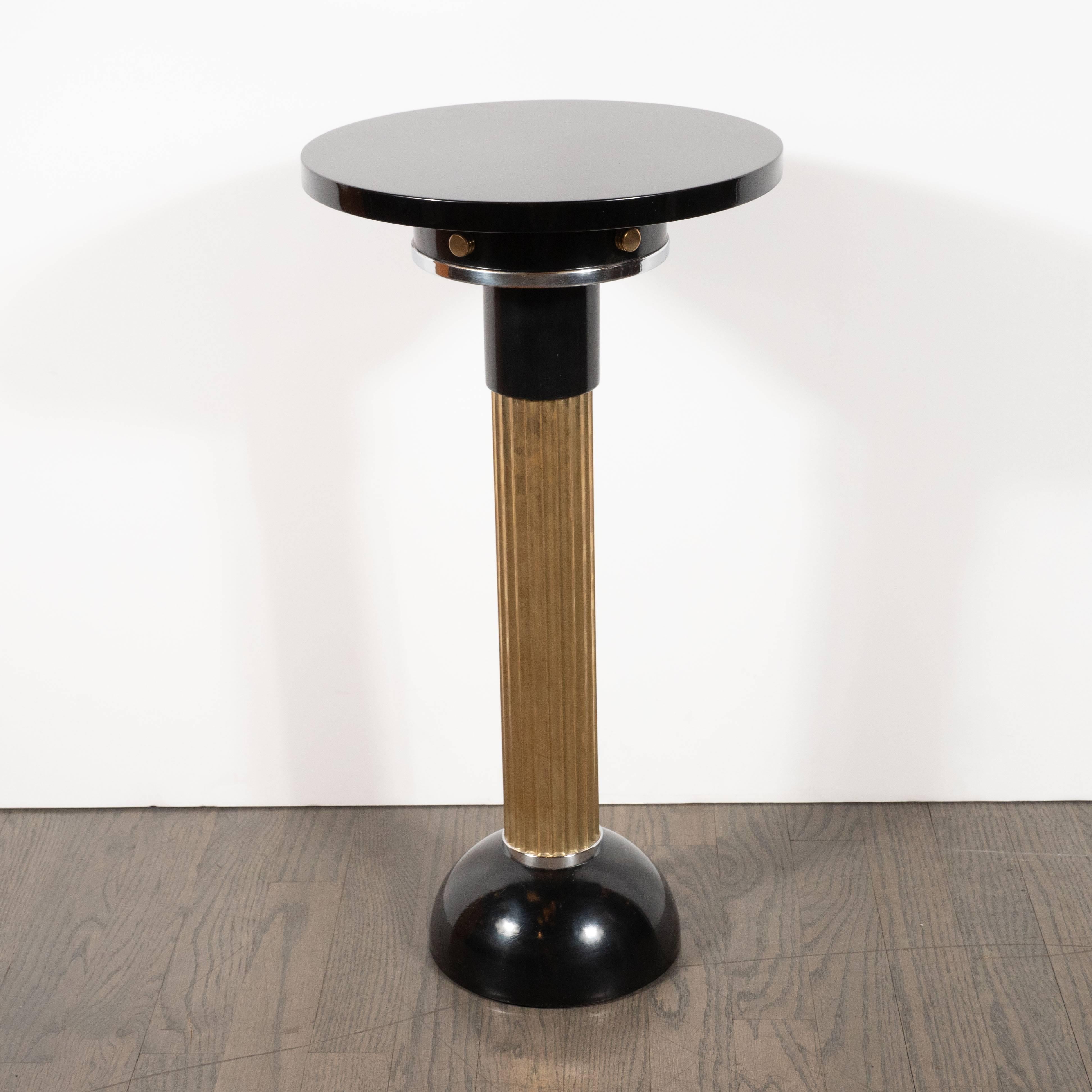 This dramatic and alluring Art Deco Machine Age drinks table was realized in the United States, circa 1935. It features a black enamel domed base; a reeded brass columnar cylindrical body and a skyscraper style top. The brass body is capped with a