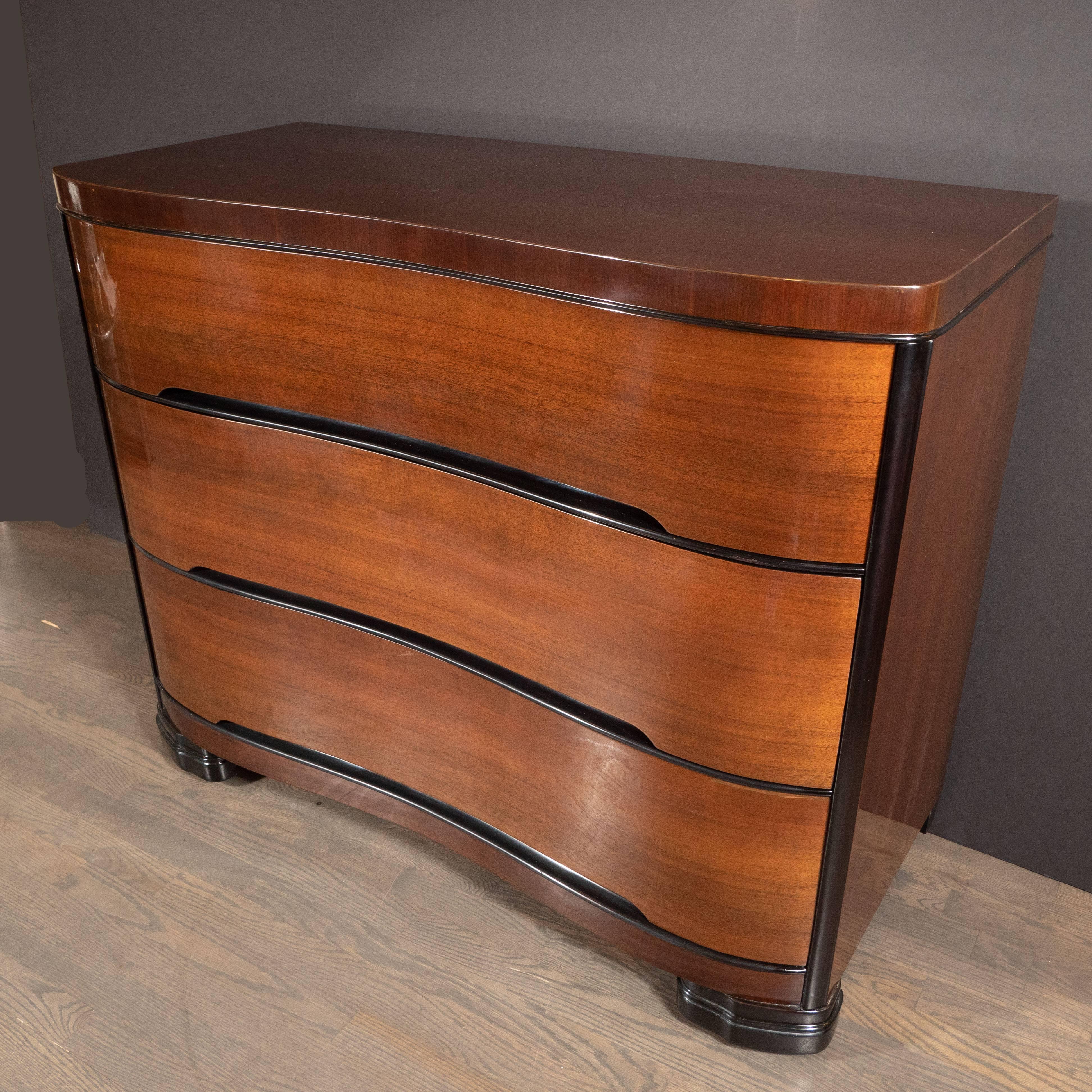 This refined chest was realized by the Tri-Bond Furniture Company in the United States, circa 1935. It features five drawers a bow-front offering sinuous curves in bookmatched mahogany with lacquer detailing tracing the top and bottom of each and