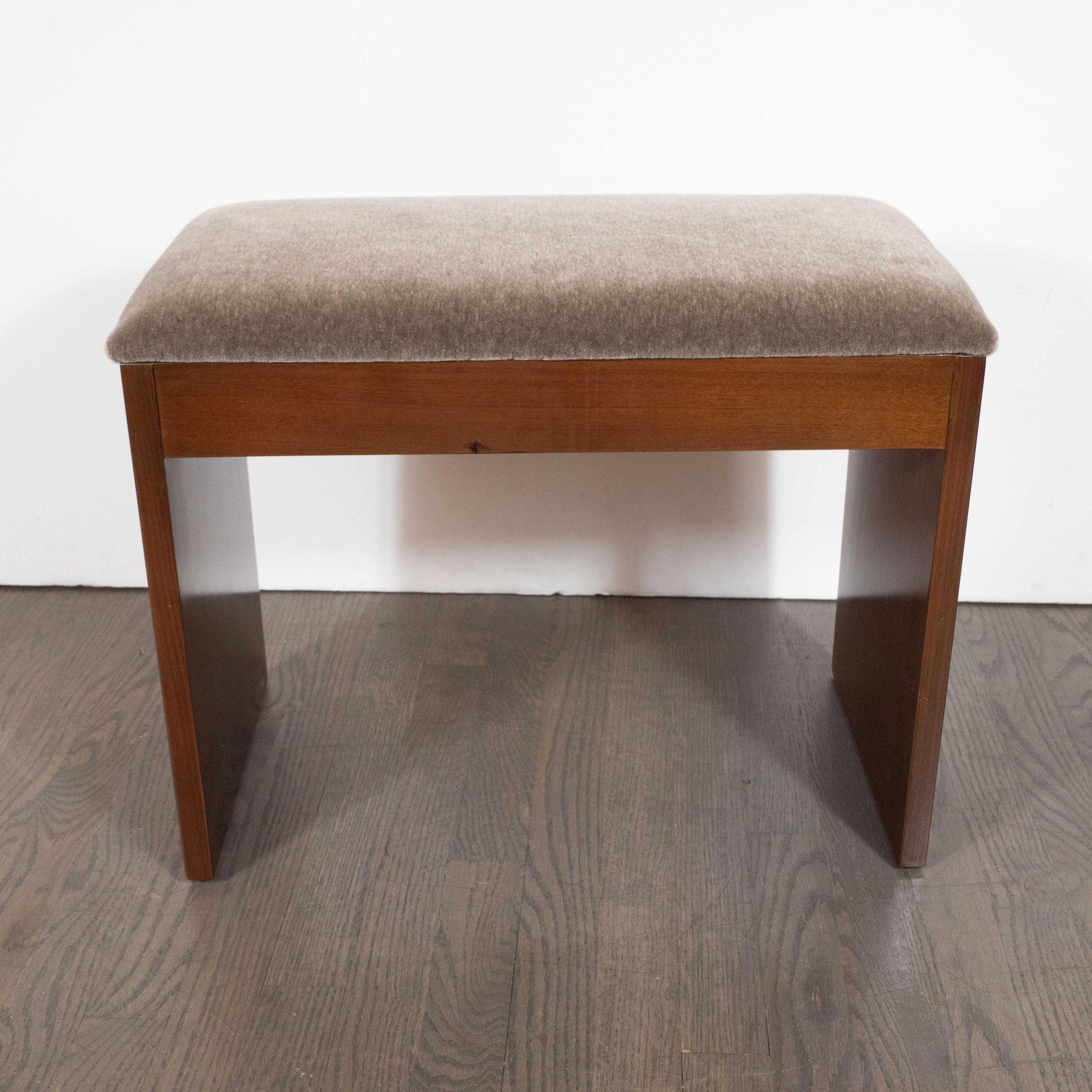 This refined Art Deco bench was realized in the United States, circa 1935. It features a rectilinear body with well attenuated and elegant proportions realized in bookmatched walnut-offering a stunning natural grain. It has been newly reupholstered