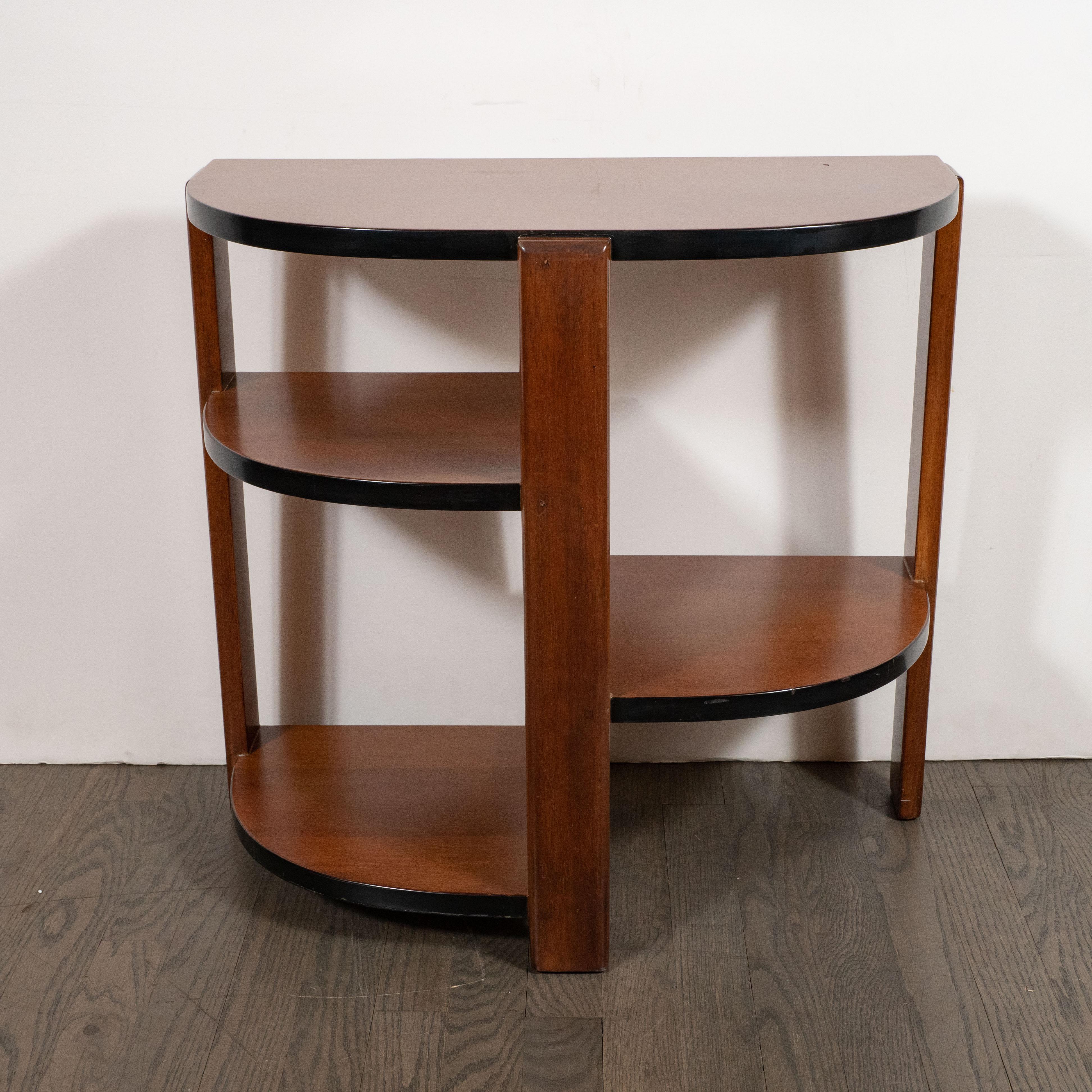 This elegant Art Deco Machine Age cubist end/side table was realized in the United States, circa 1935. It features a demilune top and three streamlined planes that connect to a central support at a perpendicular angle- all in handrubbed walnut. The