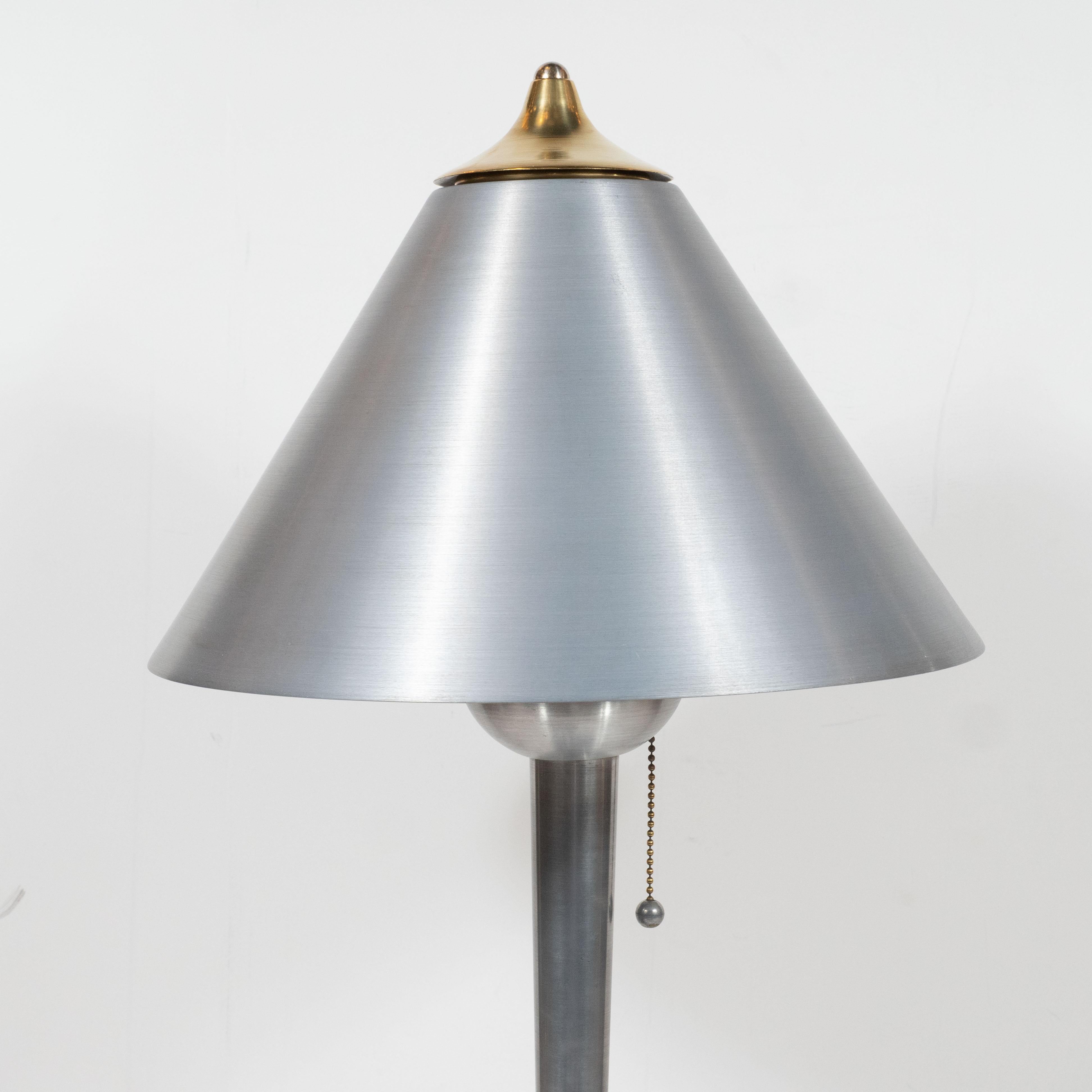 This sophisticated Art Deco Machine Age table lamp was realized in the United States, circa 1935. They feature a skyscraper style two-tiered brushed aluminum base from which a cylindrical body- flaring subtly to its apex- ascends. The body