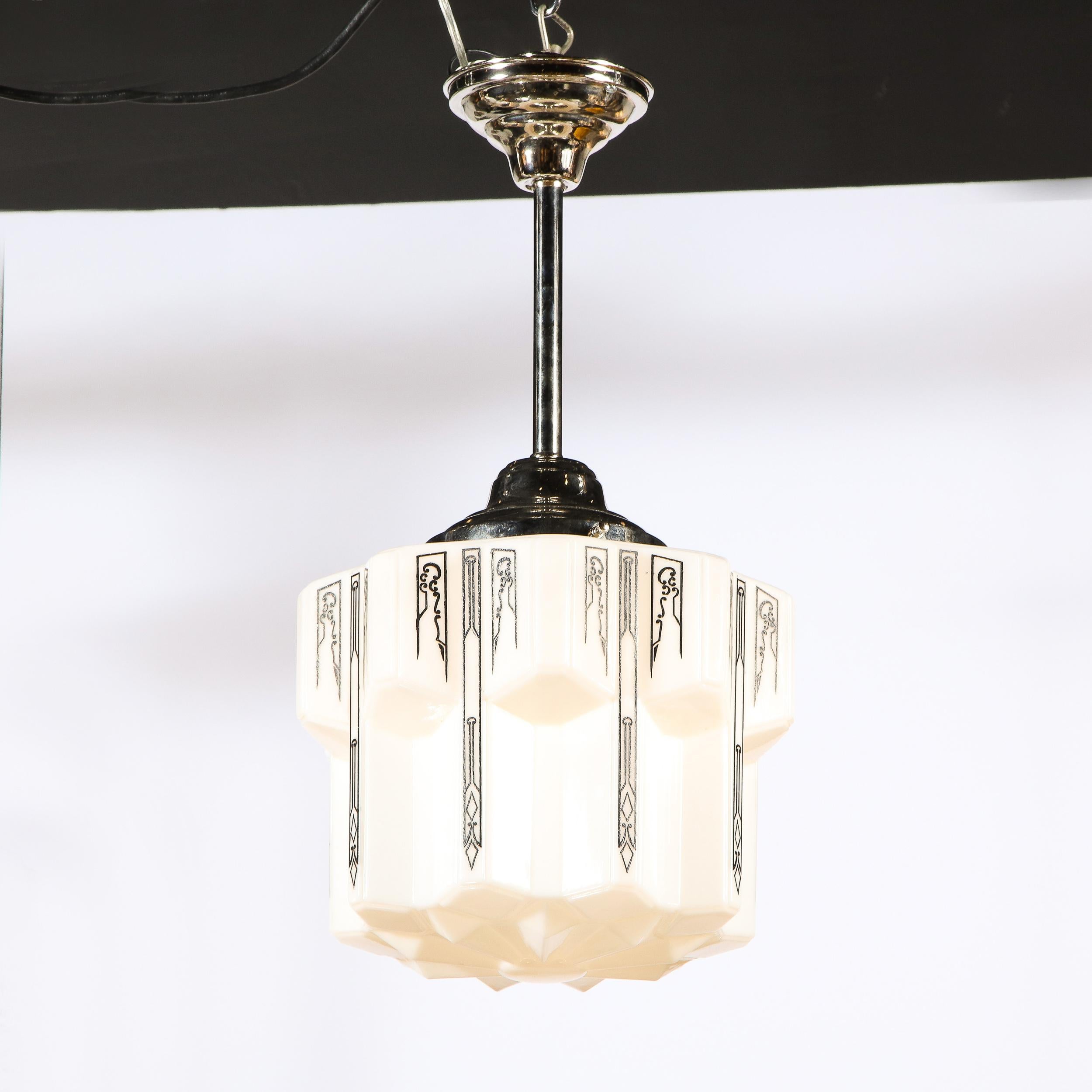 This refined and graphic Art Deco Machine Age pendant was realized in the United States circa 1935. It features a sculptural body with faceted sides adorned with abstract curvilinear detailing throughout The pendant is composed of white milk glass