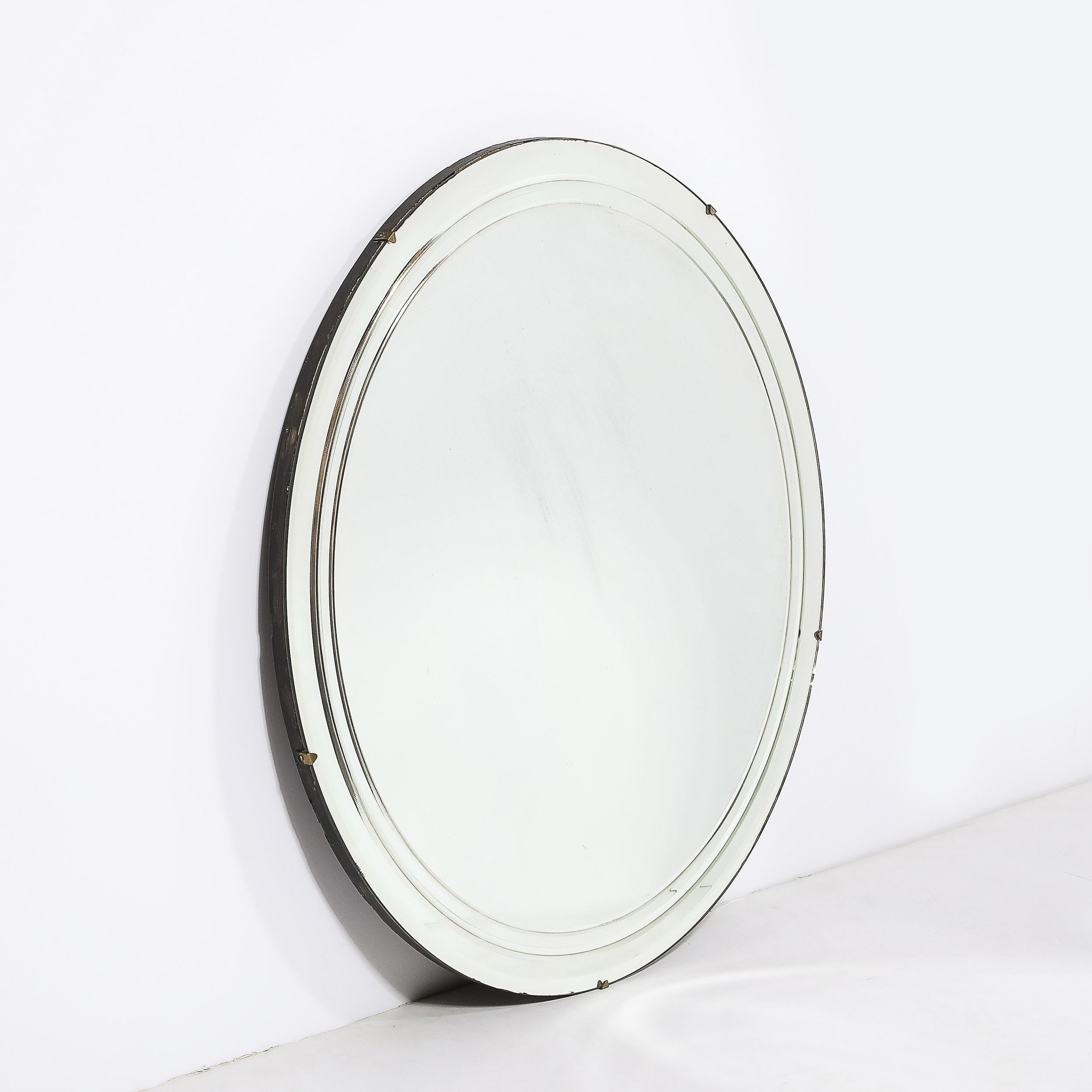 This materially dynamic and sleek Art Deco Machine Age Round Mirror W/Reverse Tiered Bevel Detailing & Brass Fittings originates from the United States, Circa 1935. Features a round silhouette beautifully scaled and proportioned, putting the
