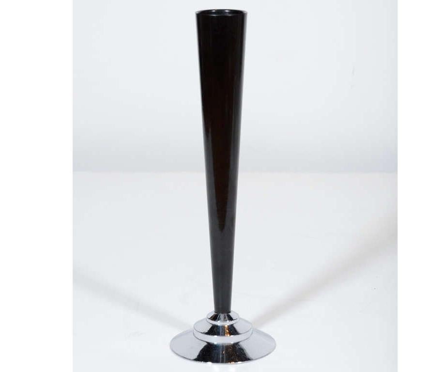This stunning Art Deco Machine Age bakelite bud vase features a slender conical body realized in black bakelite that rests atop a stepped skyscraper style base in lustrous chrome. While this is a perfectly functional item- ideal for presenting