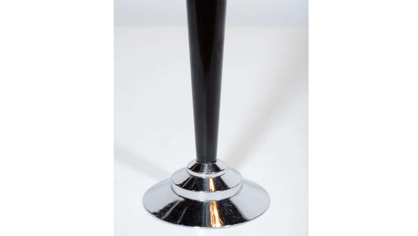 This stunning Art Deco Machine Age bakelite bud vase features a slender conical body realized in black bakelite that rests atop a stepped skyscraper style base in lustrous chrome. While this is a perfectly functional item- ideal for presenting