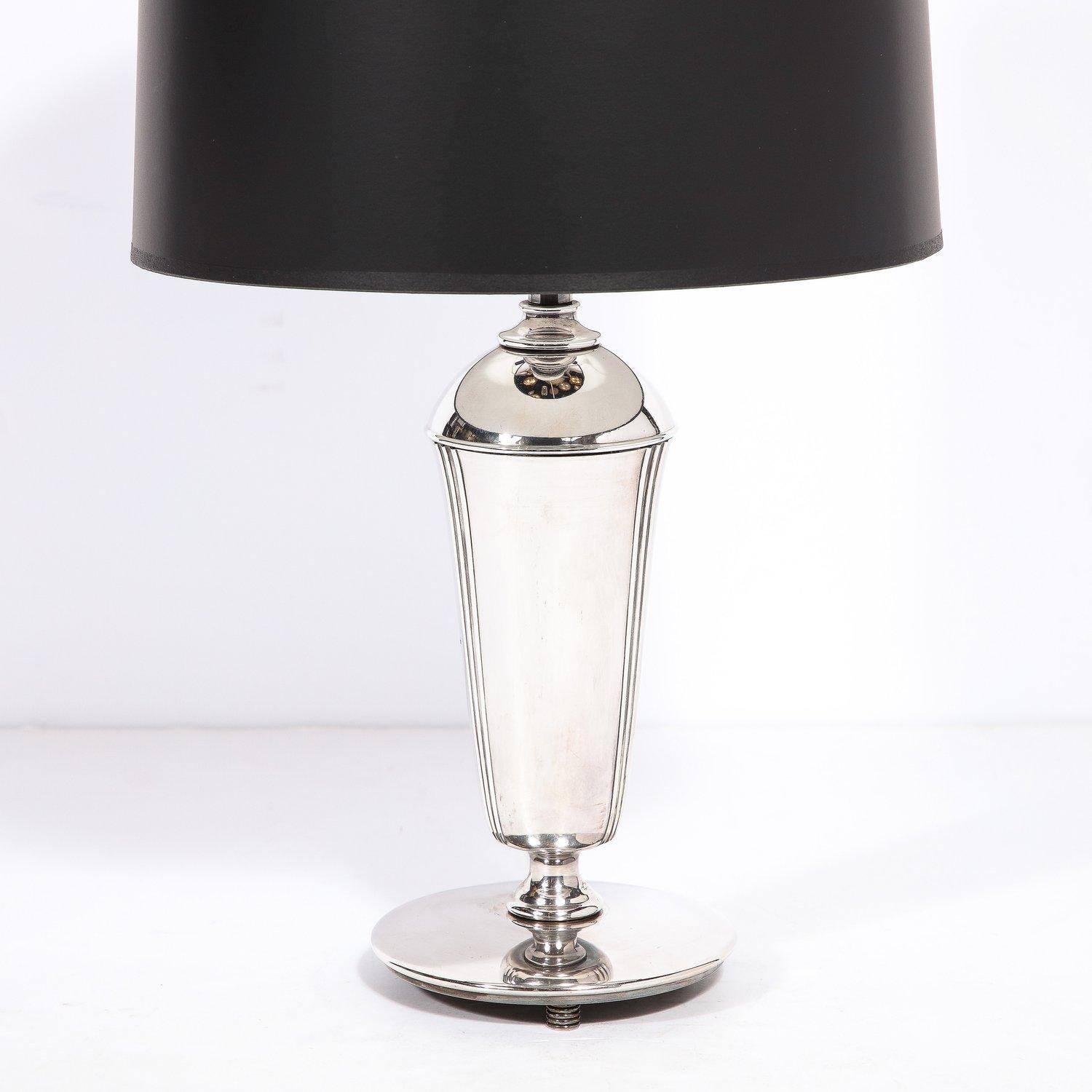 This stunning Art Deco Machine Age chrome table lamp was realized in the United States circa 1935.  Sitting on three coiled feet with horizontal bands, it features a circular base from which a elongated conical form ascends tapering at its shoulder