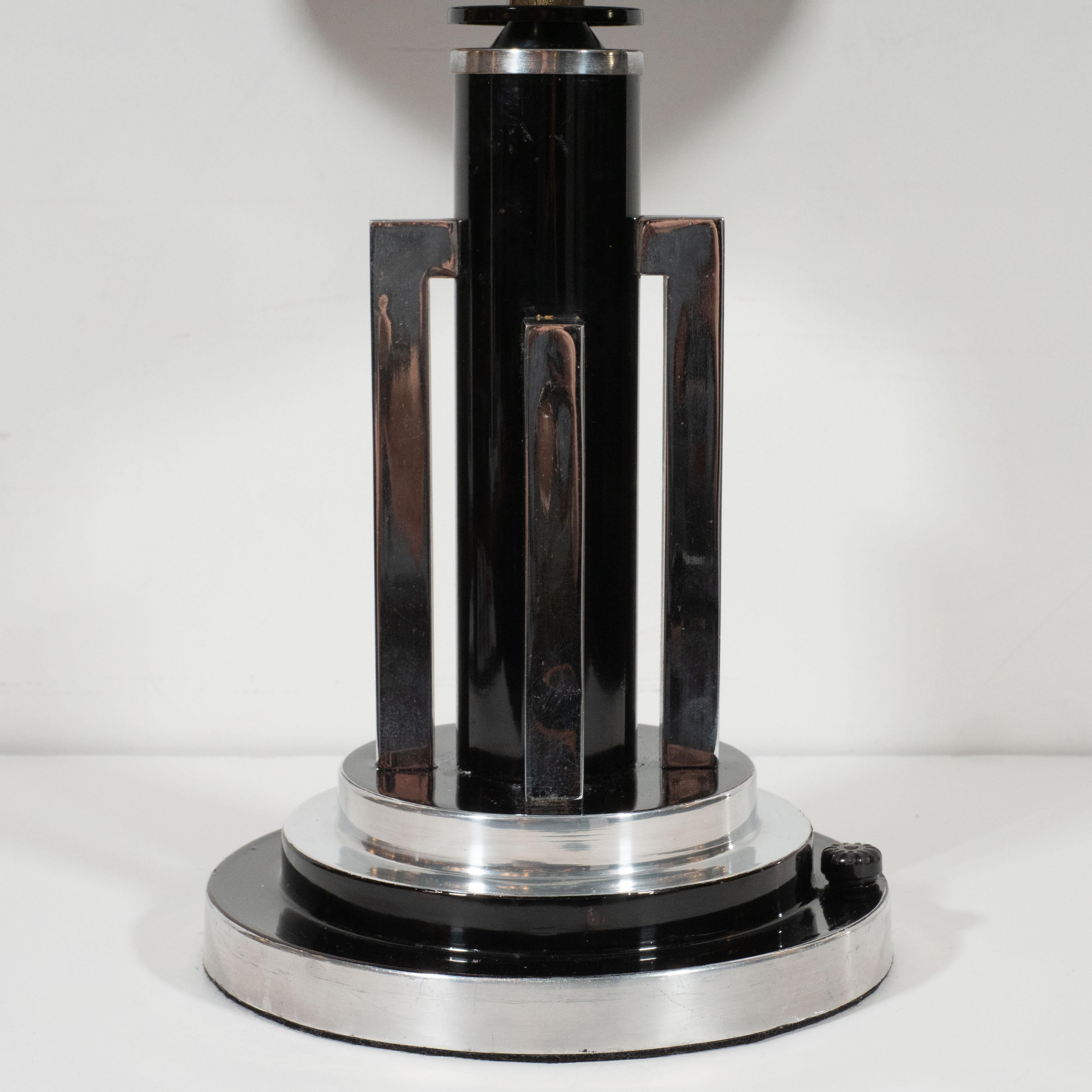 This dramatic and striking table lamp was realized in the United States, circa 1935. It features a skyscraper style base consisting of three concentric circular forms alternating between black lacquer and chrome; a cylindrical black enamel body and