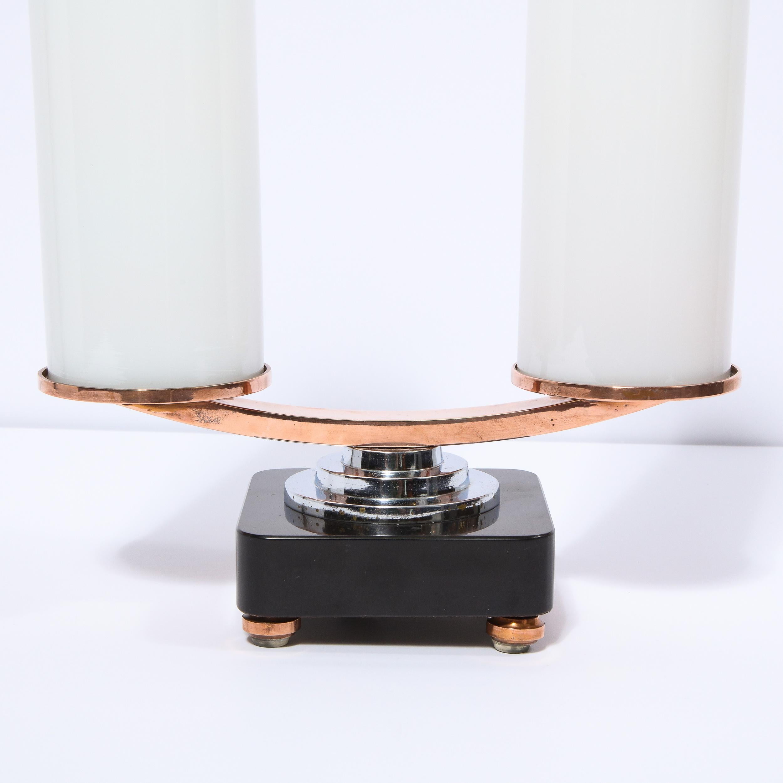This stunning Art Deco Machine Age skyscraper style streamlined table lamp was realized in the United States, circa 1935. It features a volumetric square vitrolite glass base with rounded corners and round skyscraper style chrome & copper feet. A