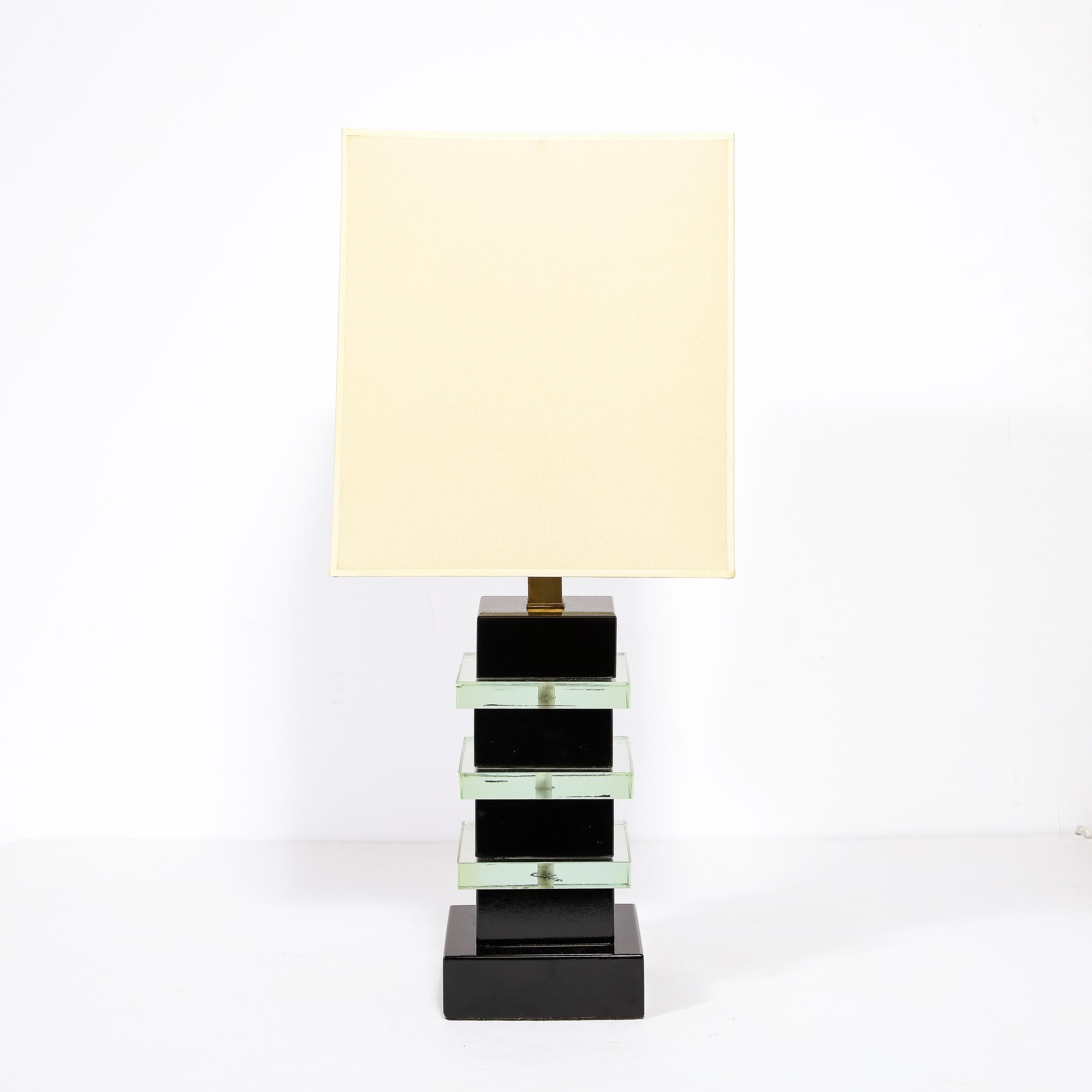 This stunning and graphic Art Deco Machine Age skyscraper style table lamp in the manner of Donald Deskey was realized in the United States circa 1935. It features a volumetric square base in black lacquer with three forms of the same shape and