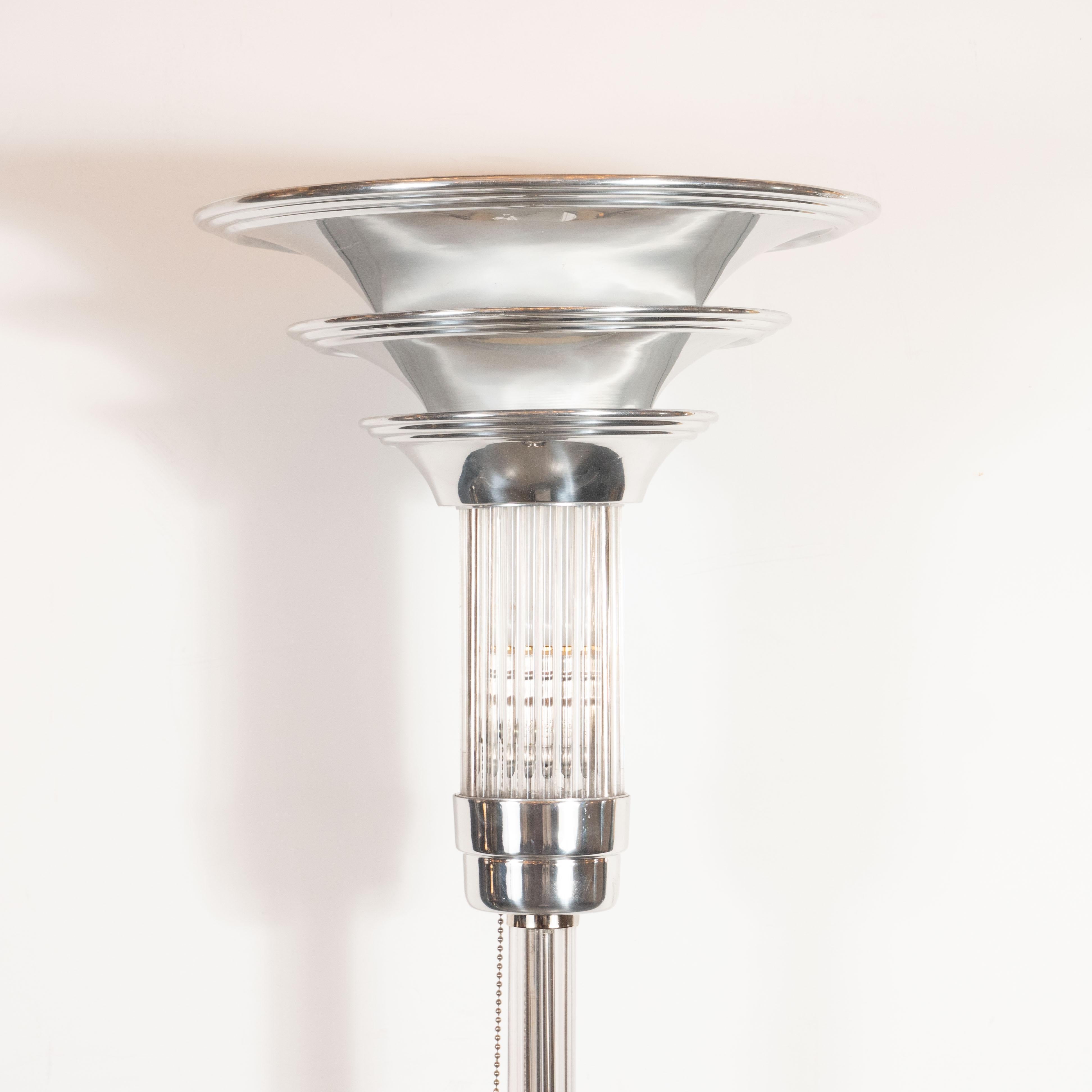 This sophisticated Art Deco Machine Age torchiere was realized in the United States, circa 1935. It features a circular base from which a cylindrical rod- all in polished nickel- ascends culminating in a dramatic skyscraper style shade consisting of