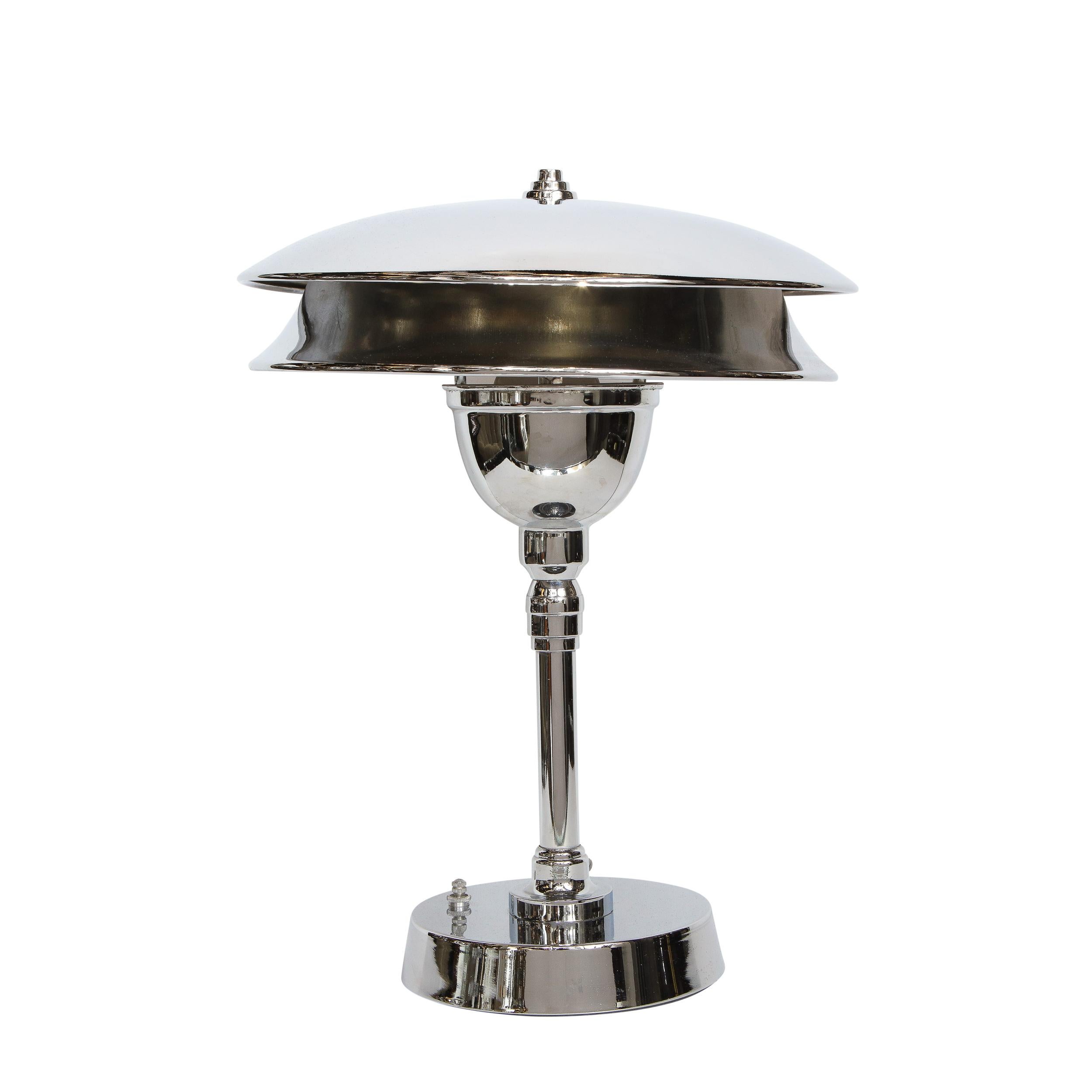 This refined Art Deco Machine Age table lamp was realized in the United States, circa 1935. It features a volumetric circular base skyscraper style base- a form that recurs in the finial atop the two tier concave shade. This skyscraper style
