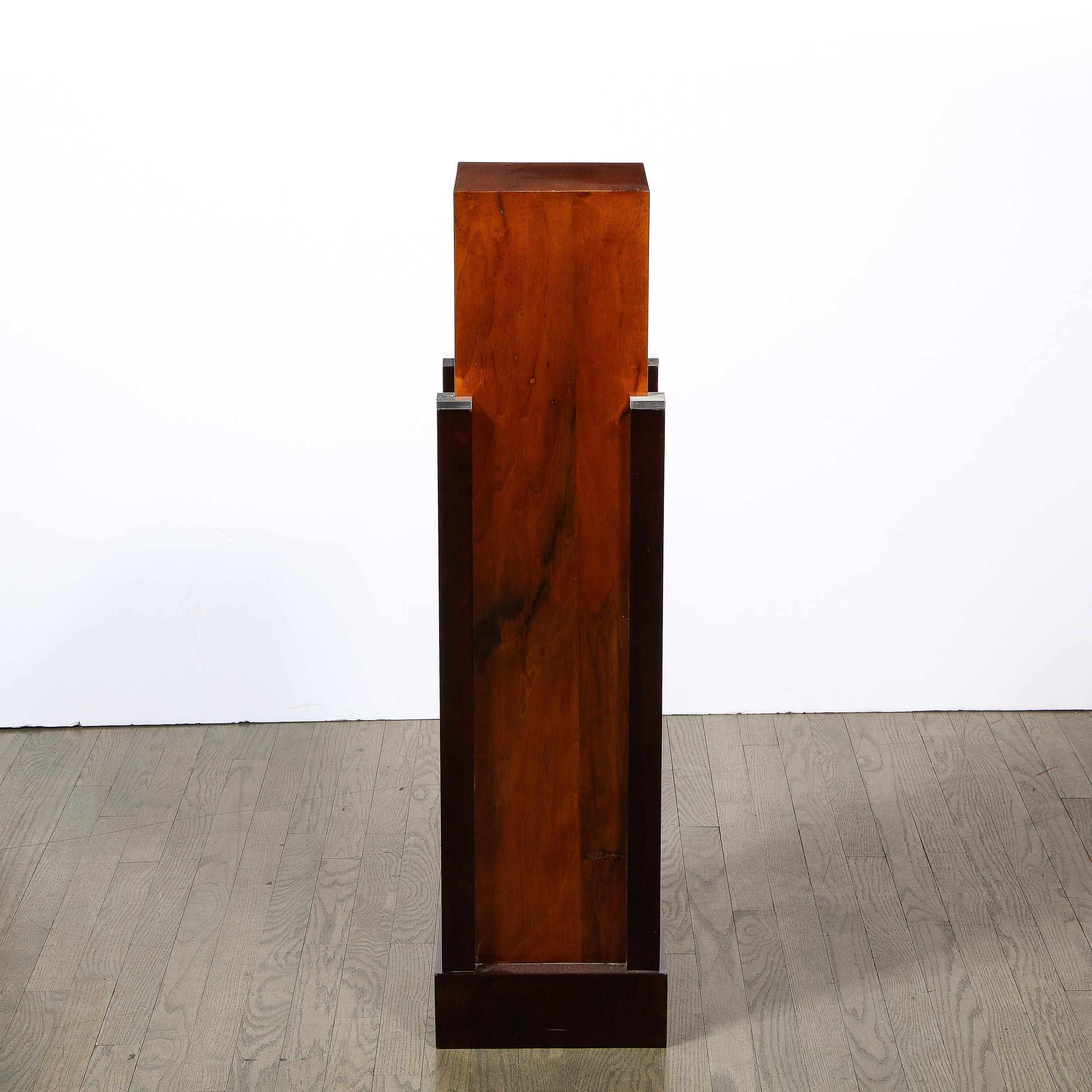 This stunning Art Deco Machine Age skyscraper style pedestal was realized in France circa 1935. It offers a black lacquer rectilinear base that surrounds the volumetric rectangular body of the pedestal composed of bookmatched walnut that exhibits a