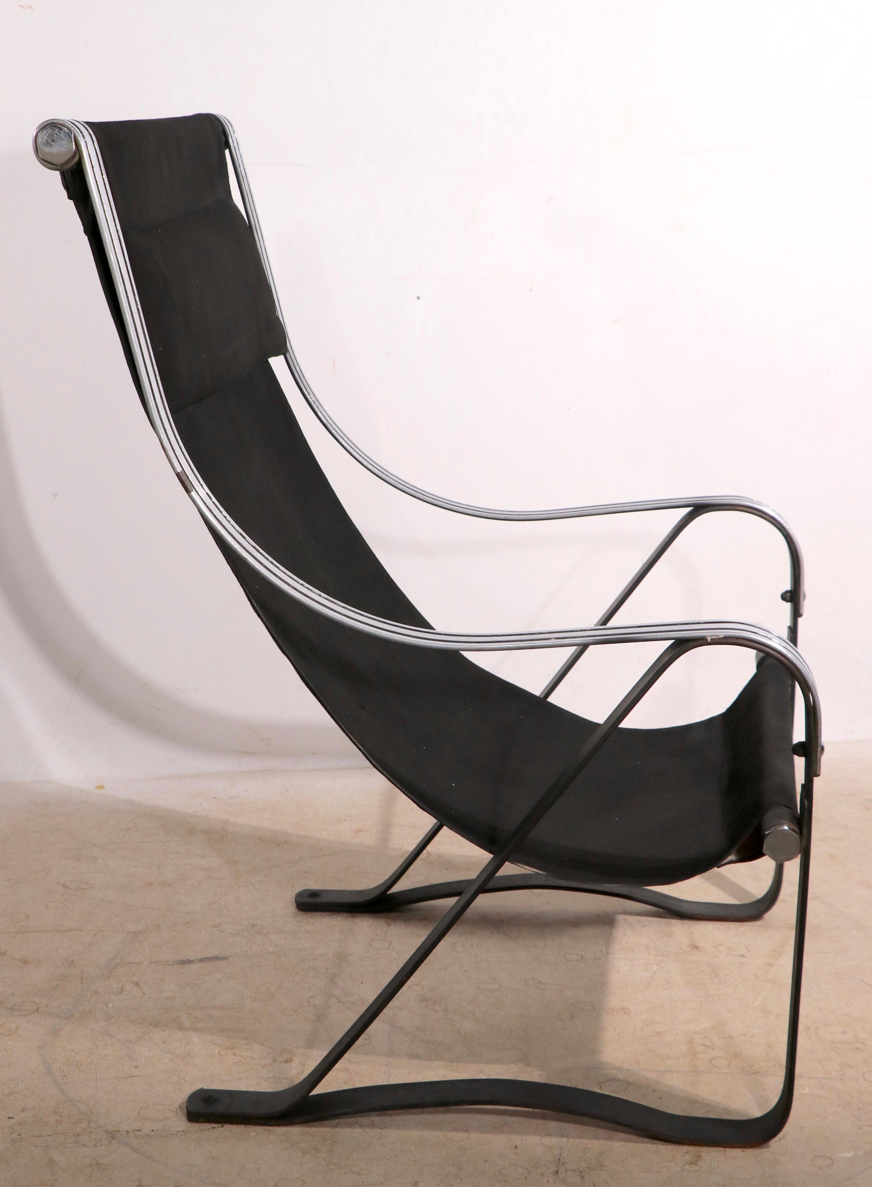 Iconic Art Deco, Machine Age sling seat lounge chair having elegant chrome and black arms on a blacked steel spring base. The chair is in overall very good condition, the chrome is bright and shiny, it shows one inconsequential flaw ( loss of