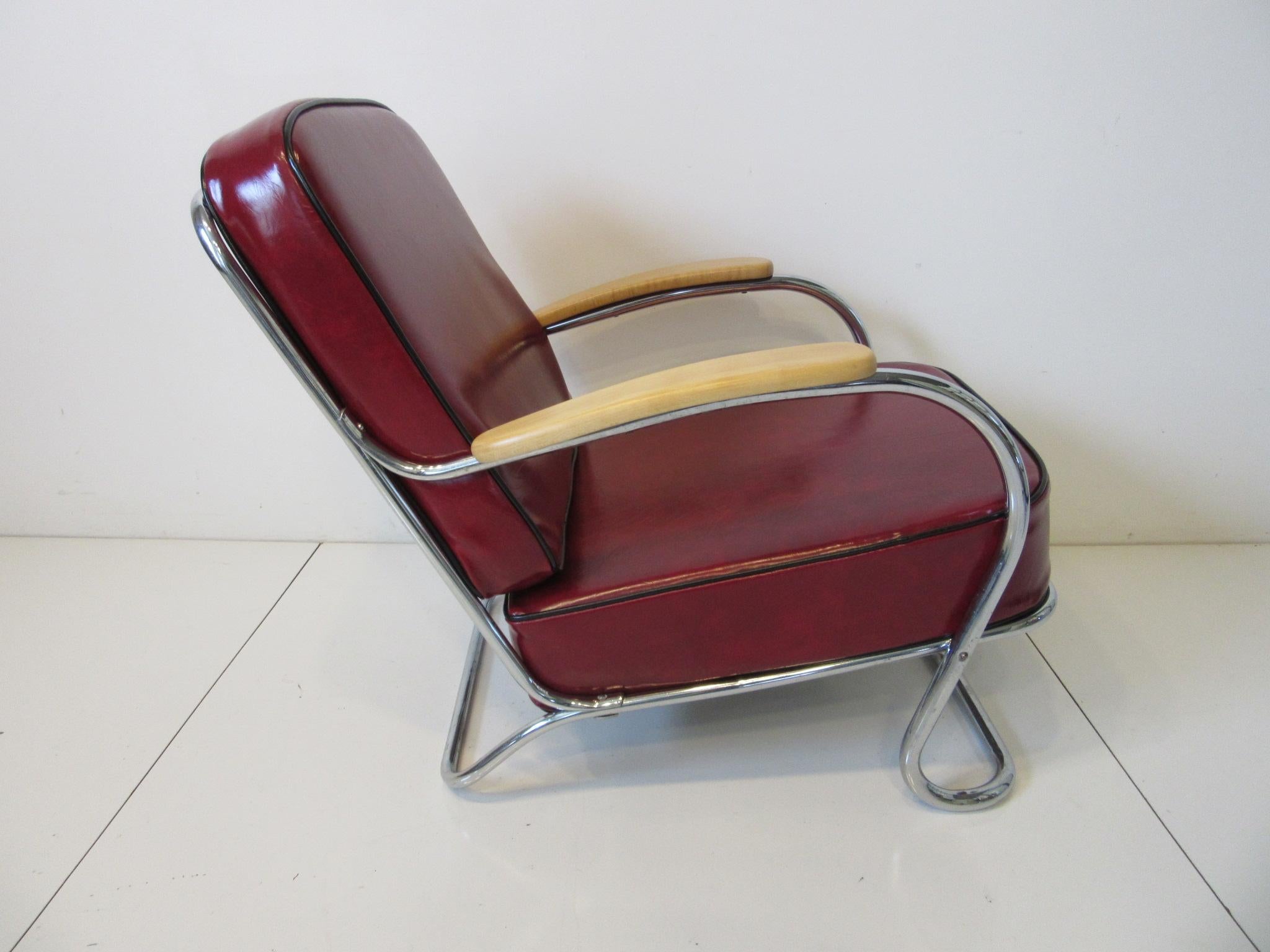 A smaller scale sculptural chrome metal tubed lounge chair with two red leatherette upholstered cushions edged in black piping. Having clear wood arm rests designed in the manner of Wolfgang Hoffmann and the Howell Furniture company.