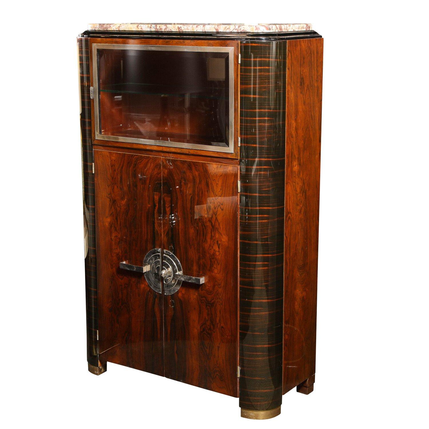 This illuminated cabinet in made of bookmatched rosewood, Macassar and mahogany woods with exotic marble top and polished nickel machine age pulls of concentric banded circles. The door features a hand beveled original glass door with glass shelf,