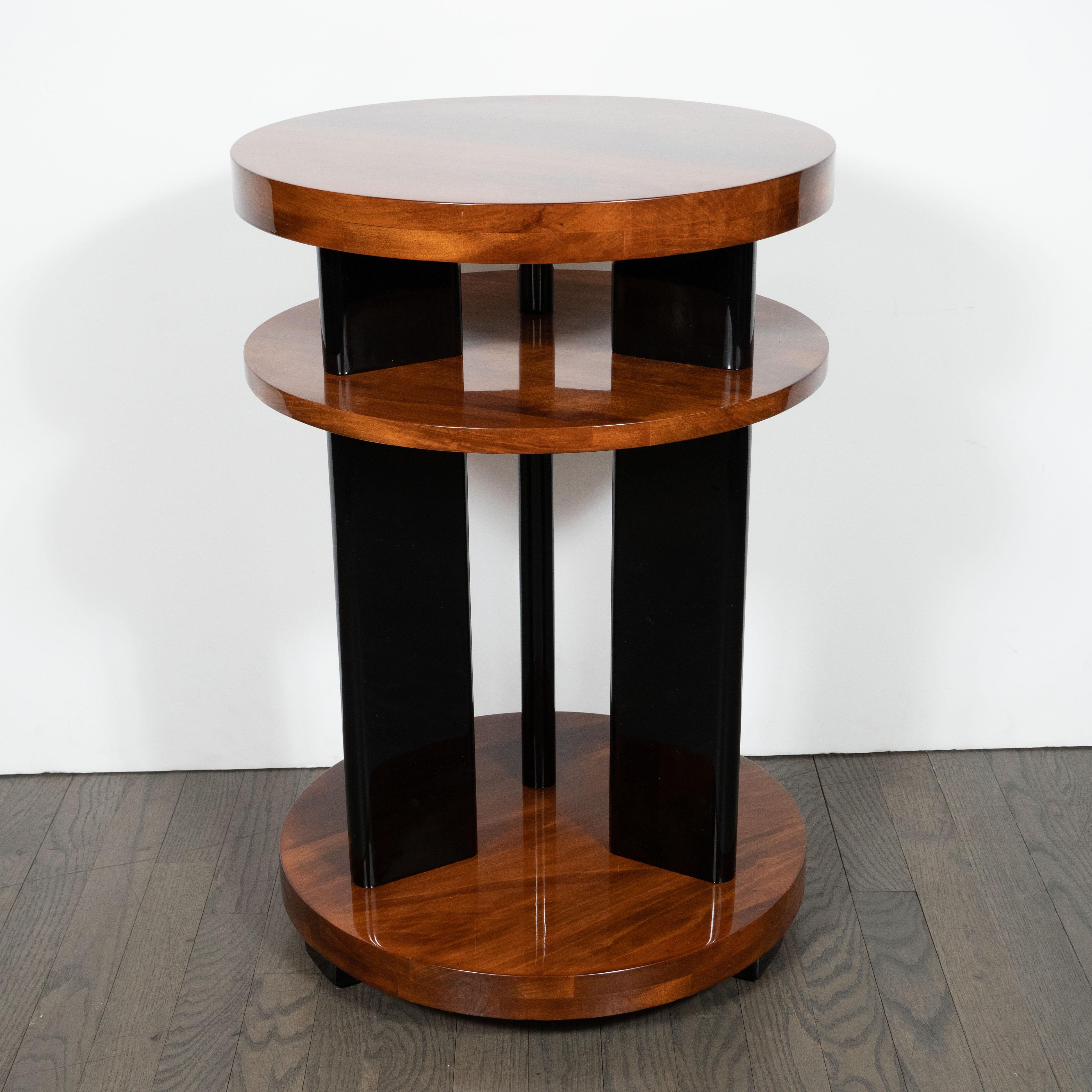 This elegant Art Deco Machine Age side table was realized in the United States, circa 1935. It features three circular tiers in bookmatched walnut connected by three streamlined rectangular supports in black lacquer that appear to pierce the centre