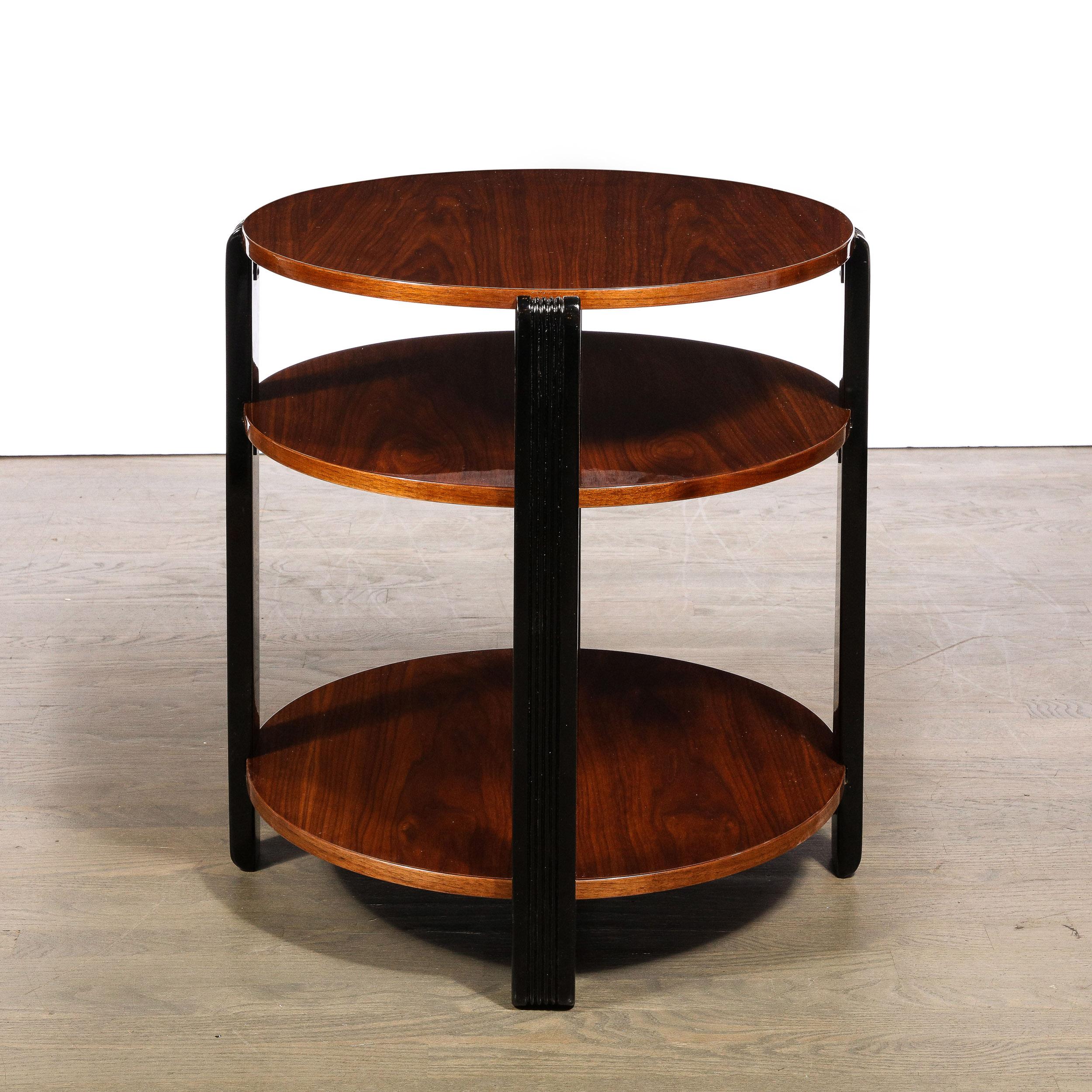 This elegant Art Deco machine age occasional table was realized in the United States circa 1935. It features three asymmetrically spaced tiers of beautiful bookmatched walnut connected by four lustrous black lacquer supports with vertical striated