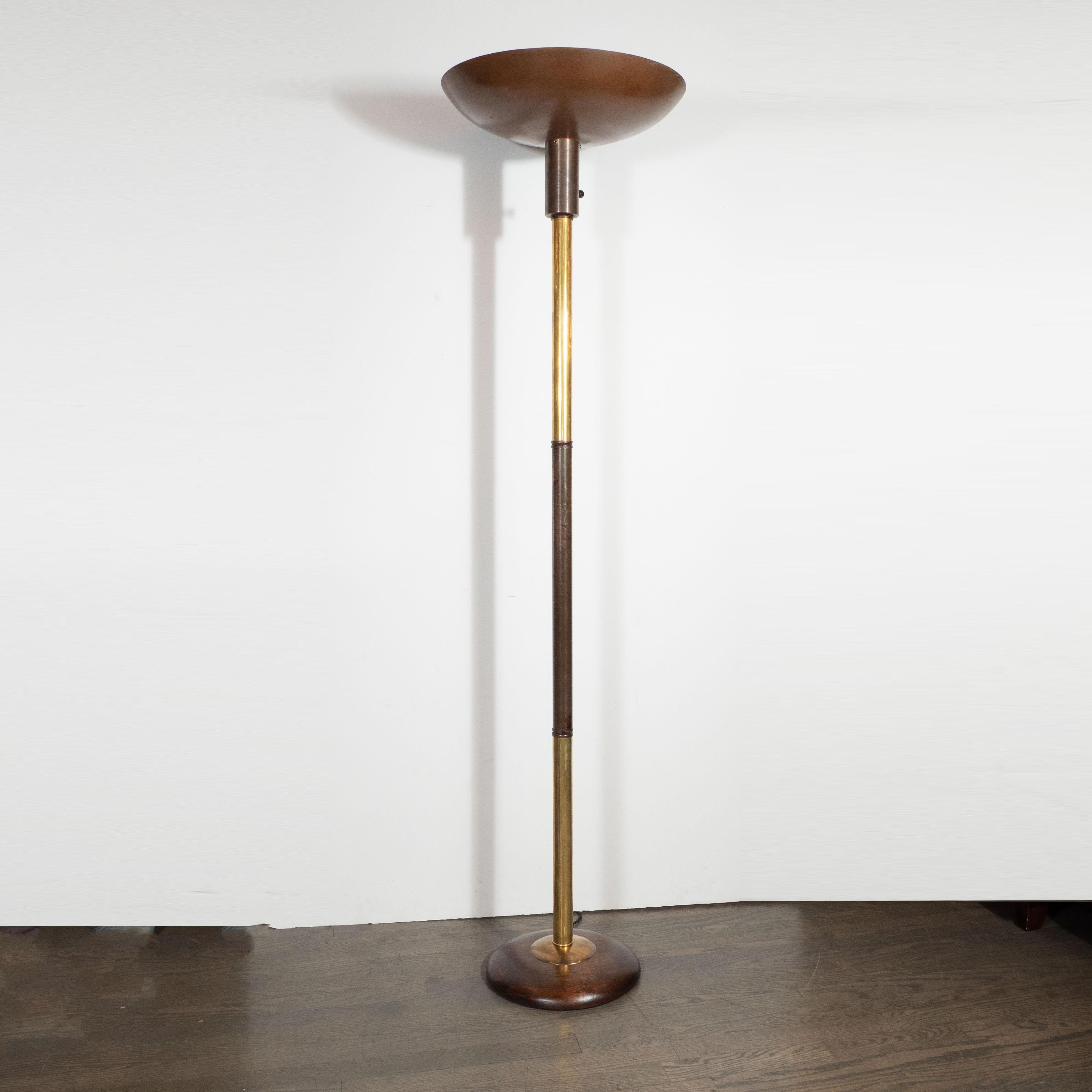 This refined Art Deco Machine Age torchiere was realized by the legendary designer, Russell Wright, in the United States circa 1940. It features a slightly convex circular base from which a central rod in alternating sections of brass and patinated