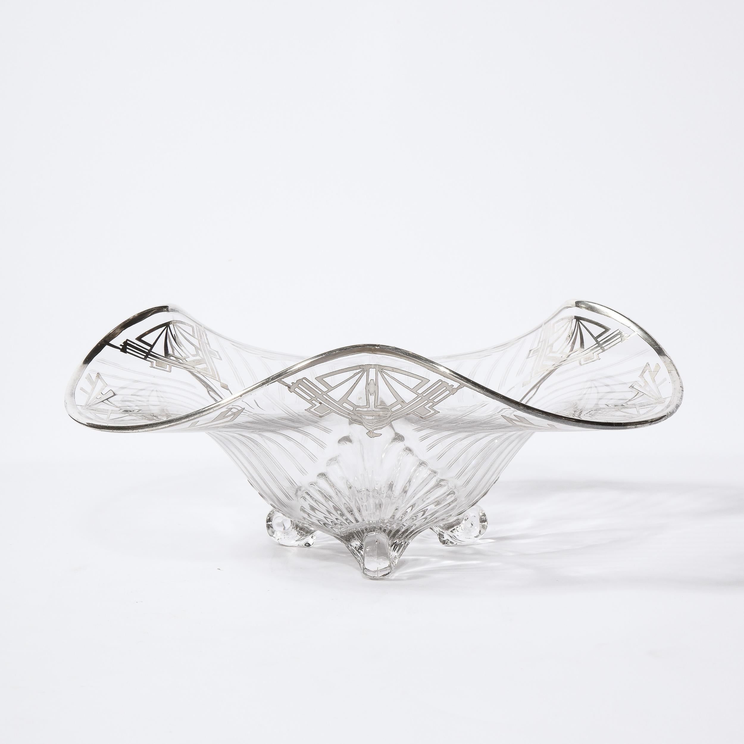 This stunning Art Deco Machine Age center bowl was realized in the United States circa 1935. It features sculptural translucent scroll form feet; an undulating curved top rimmed in sterling silver and stylized geometric detailing featuring diamond