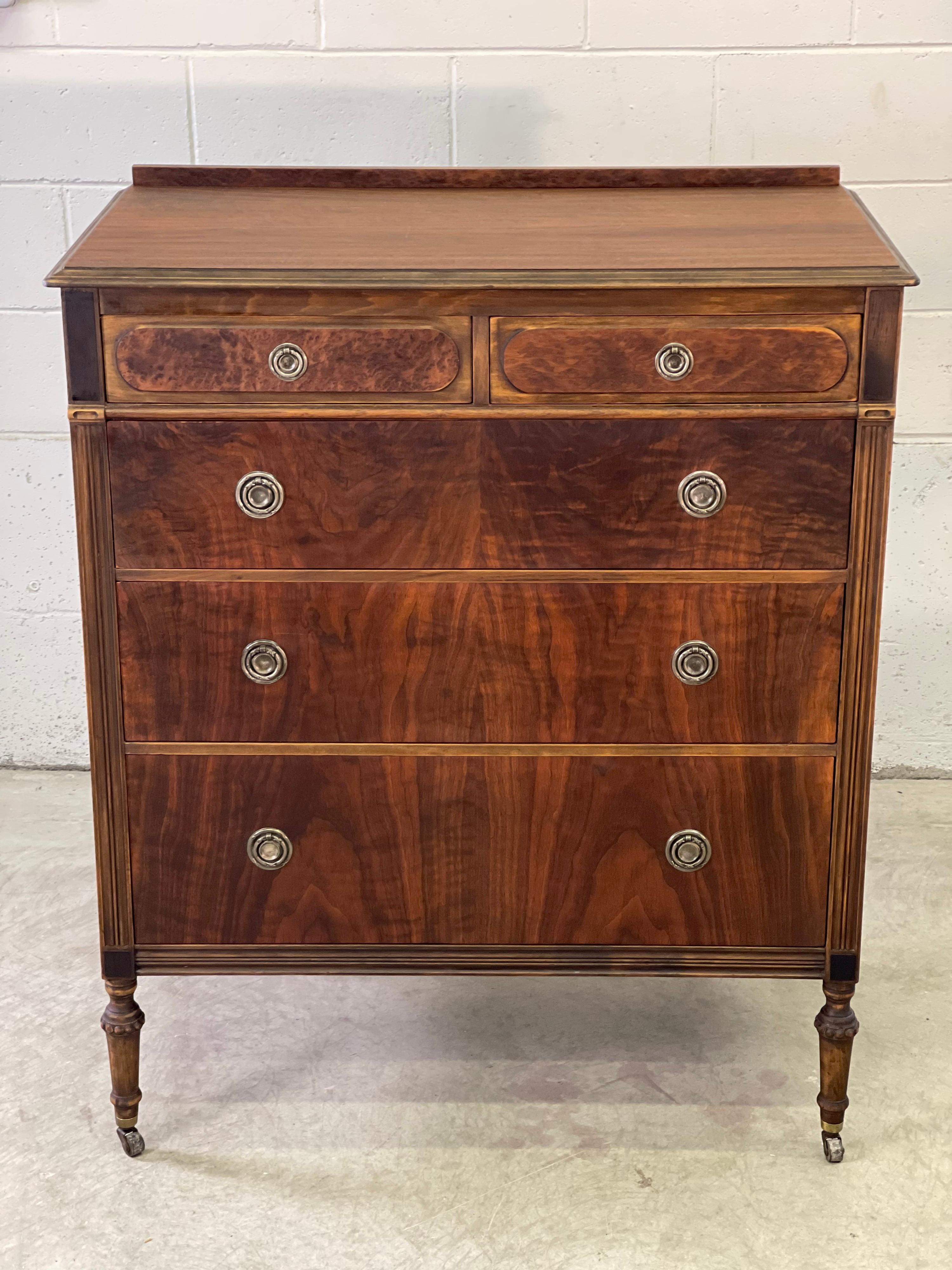 Art Deco style mahogany dresser with a flame design by Paine Furniture Co. The dresser has five drawers for storage. Two drawers on top with three larger drawers on the bottom. The drawers have round silver-tone pulls and the dresser is on castors.