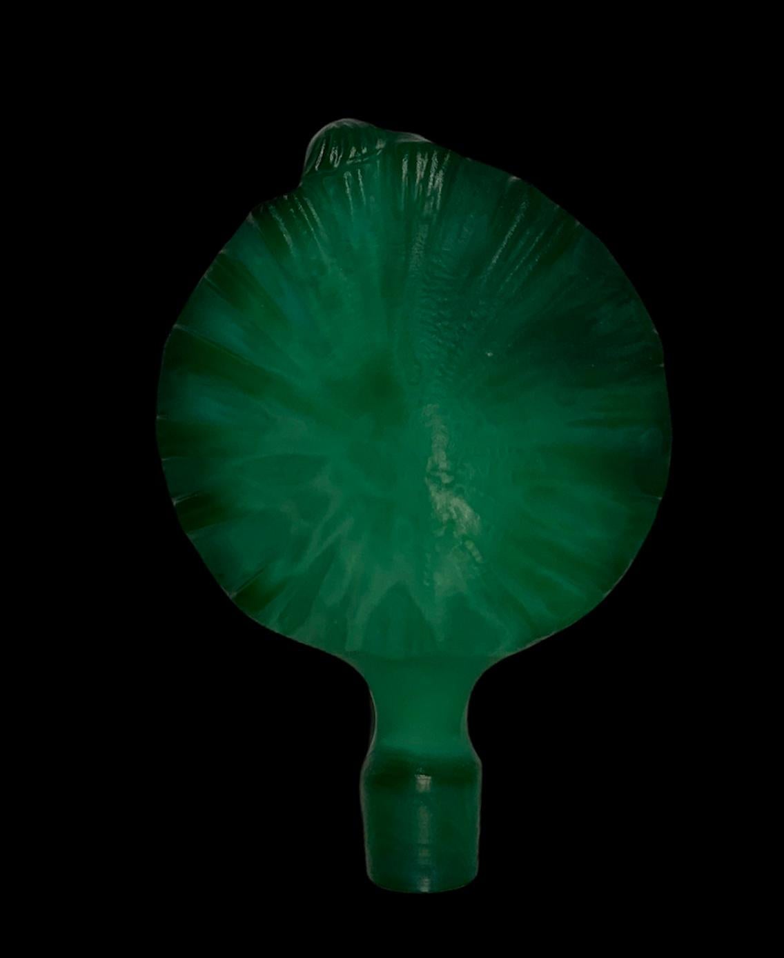 This is a malachite asymmetrical faceted perfume bottle. The stopper of the bottle is depicting a nude lady in kneeling position against a seashell holding a pearl necklace behind her back.
