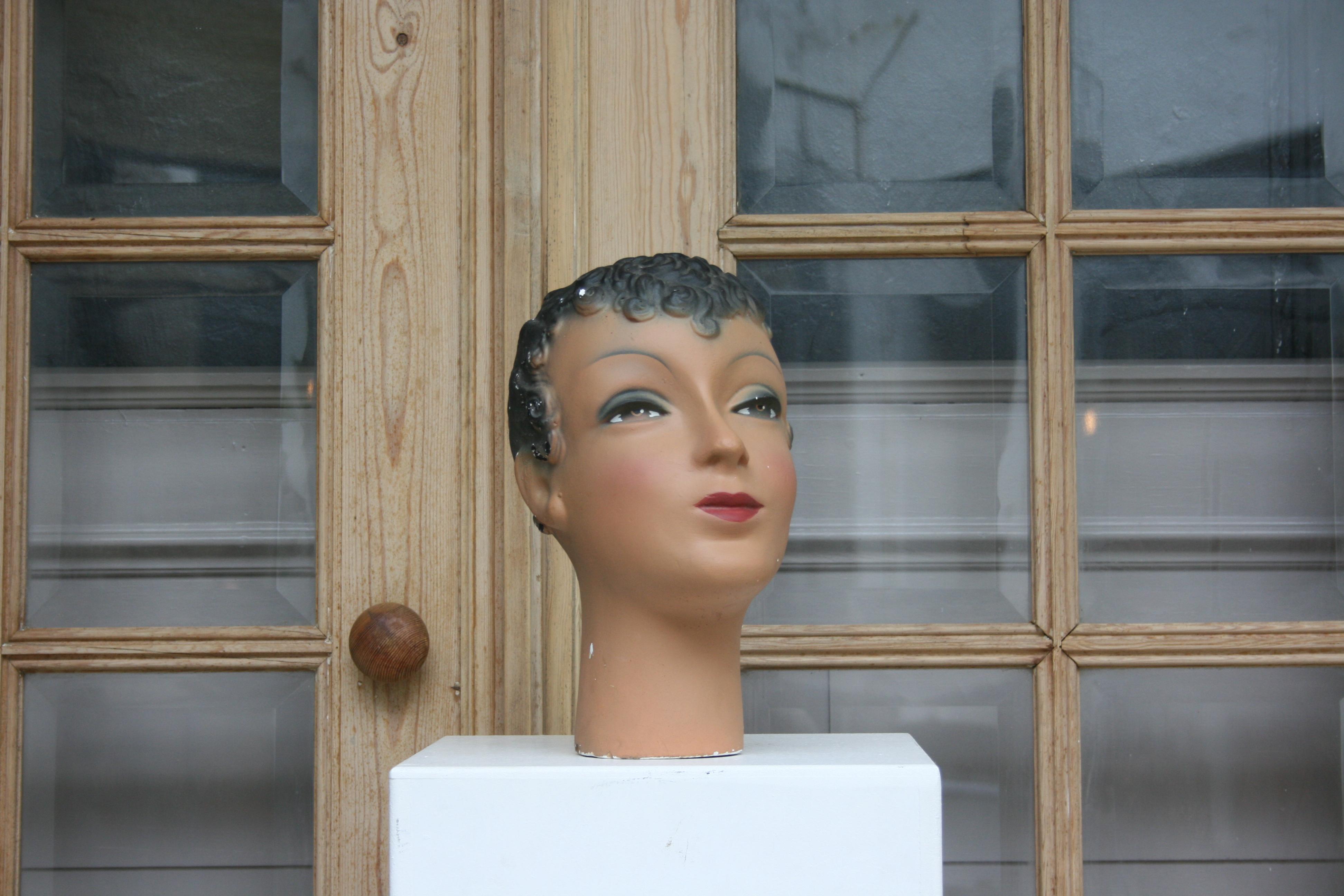 Die Schaufensterpuppe einer jungen Dame aus Brüssel in Belgien stammt aus den 30er Jahren des 20. Jahrhunderts und ist aus Gips gefertigt. Es ist polychrom bemalt. Die Dame ist geschminkt und hat geschminkte Augen. Die Marke 