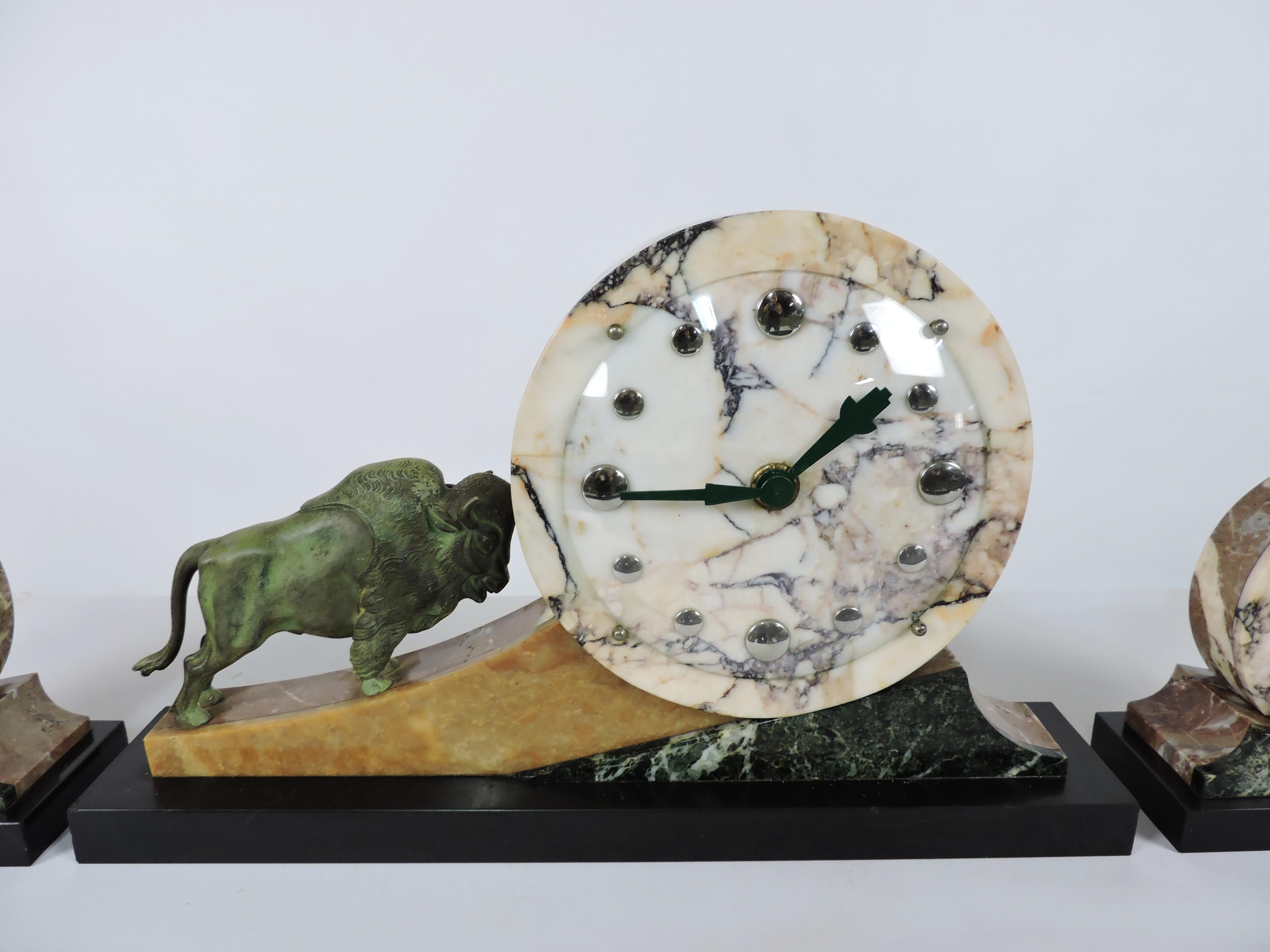 Beautiful Art Deco 3 piece mantel clock, most likely French. This high quality clock has a carved marble geometric design with a finely cast bronze bull on one side and includes 2 matching garnitures. The clock dial has a curved glass cover over it,