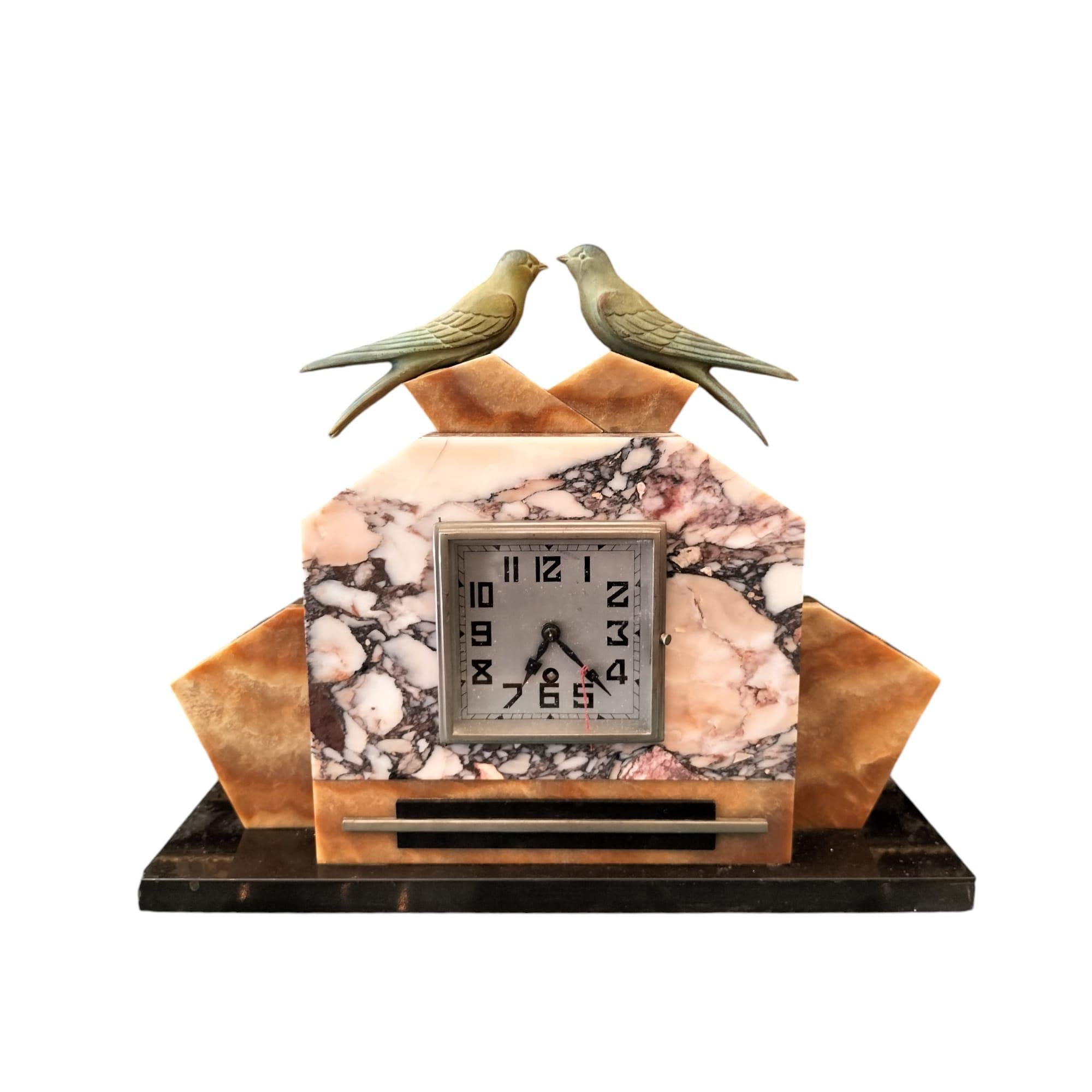 We present you with this lovely mantel clock in the style of Art Deco and hailing from the 1930s. 

It is made in marble and rests on a base made of onyx, giving it a luxurious appearance. The clock face is enclosed in a square frame with black,