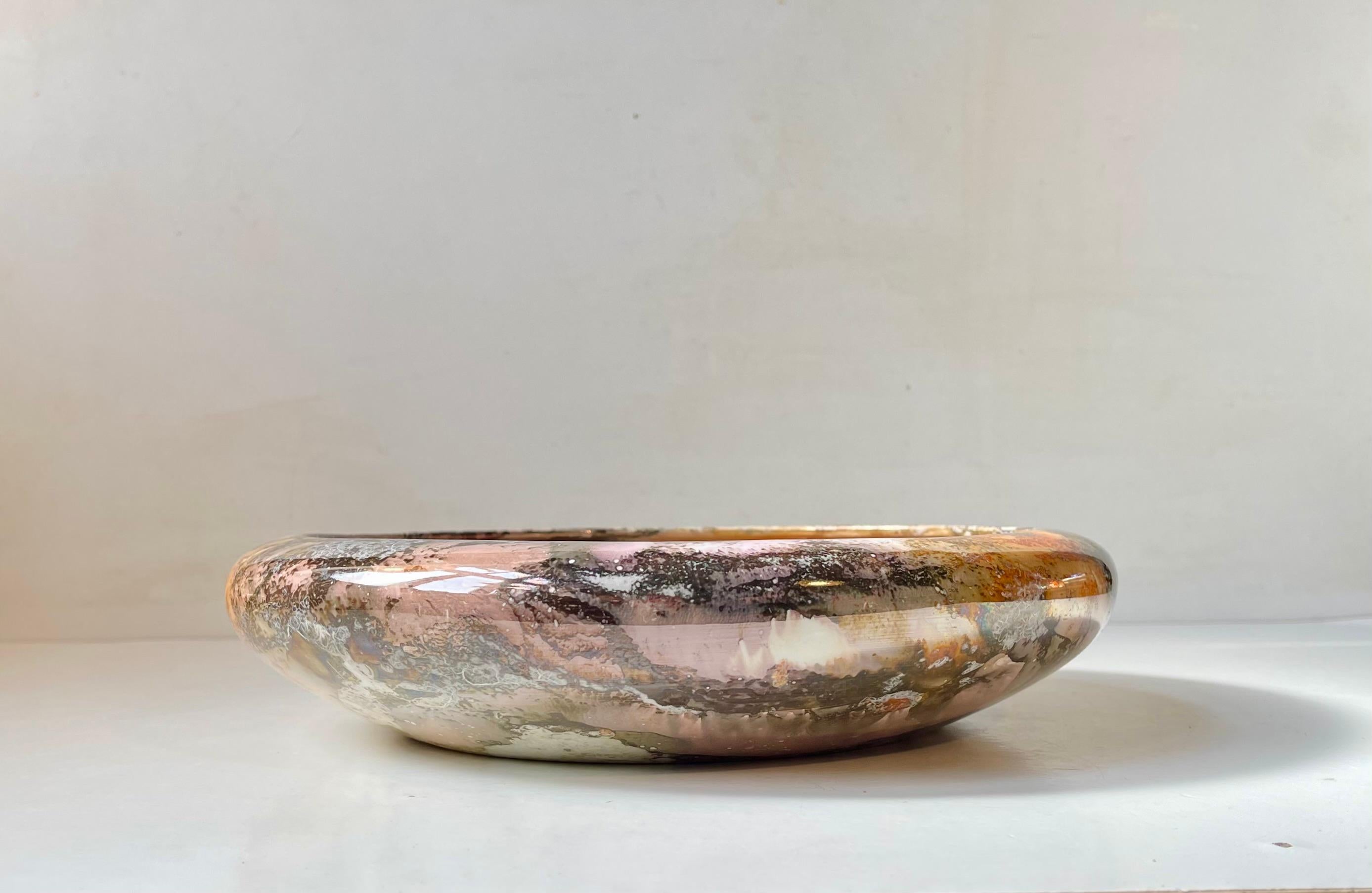 Exceptional centerpiece bowl decorated in marbled lustre glazes. Its made from faience/ceramic and the color palet burst out in a vibrancy of pink, orange, brown, black, grey and white. Designed and made by Arabia in Finland during the late 1920s.