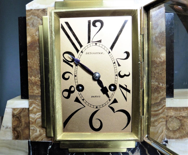 Classic Art Deco mantle clock standing on a beige marble base with black inserts. 

A gilded dog is leaping over the clock. Gilded dial with ‘Deco’ numerals and original ‘Deco’ hands signed ‘Desoutter, Paris’. 

Eight day Frech movement stamped