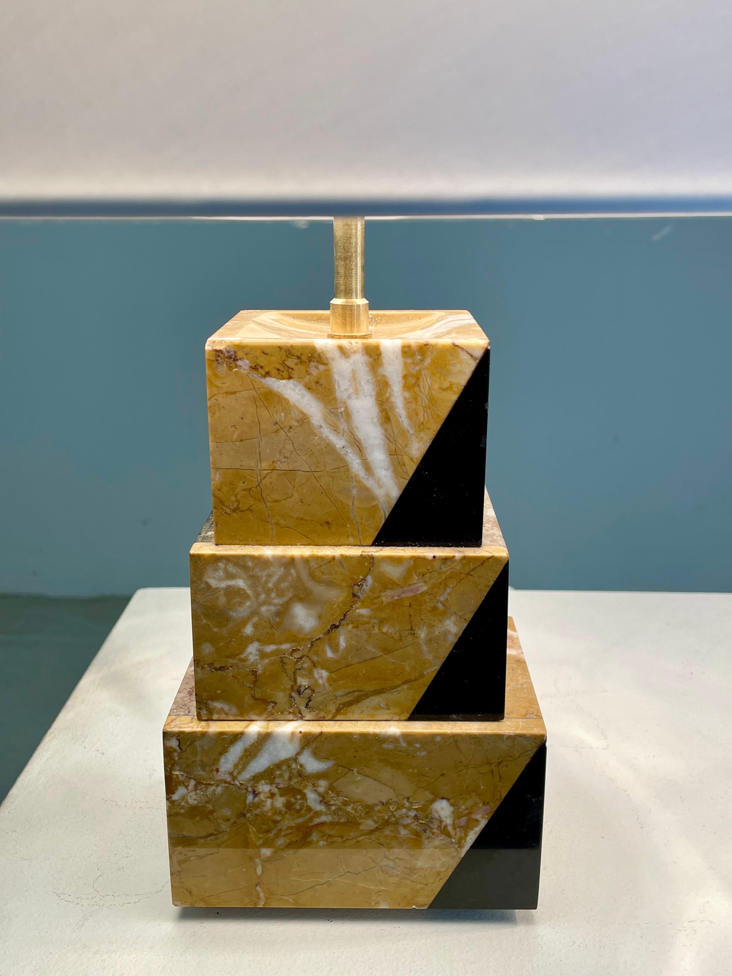 Un exquisito par de lámparas de la época Art Déco, realizadas en marquetería de mármol. Cada base está compuesta por bloques geométricos de mármol amarillo veteado, realzados con incrustaciones de mármol negro, que crean un llamativo contraste y un