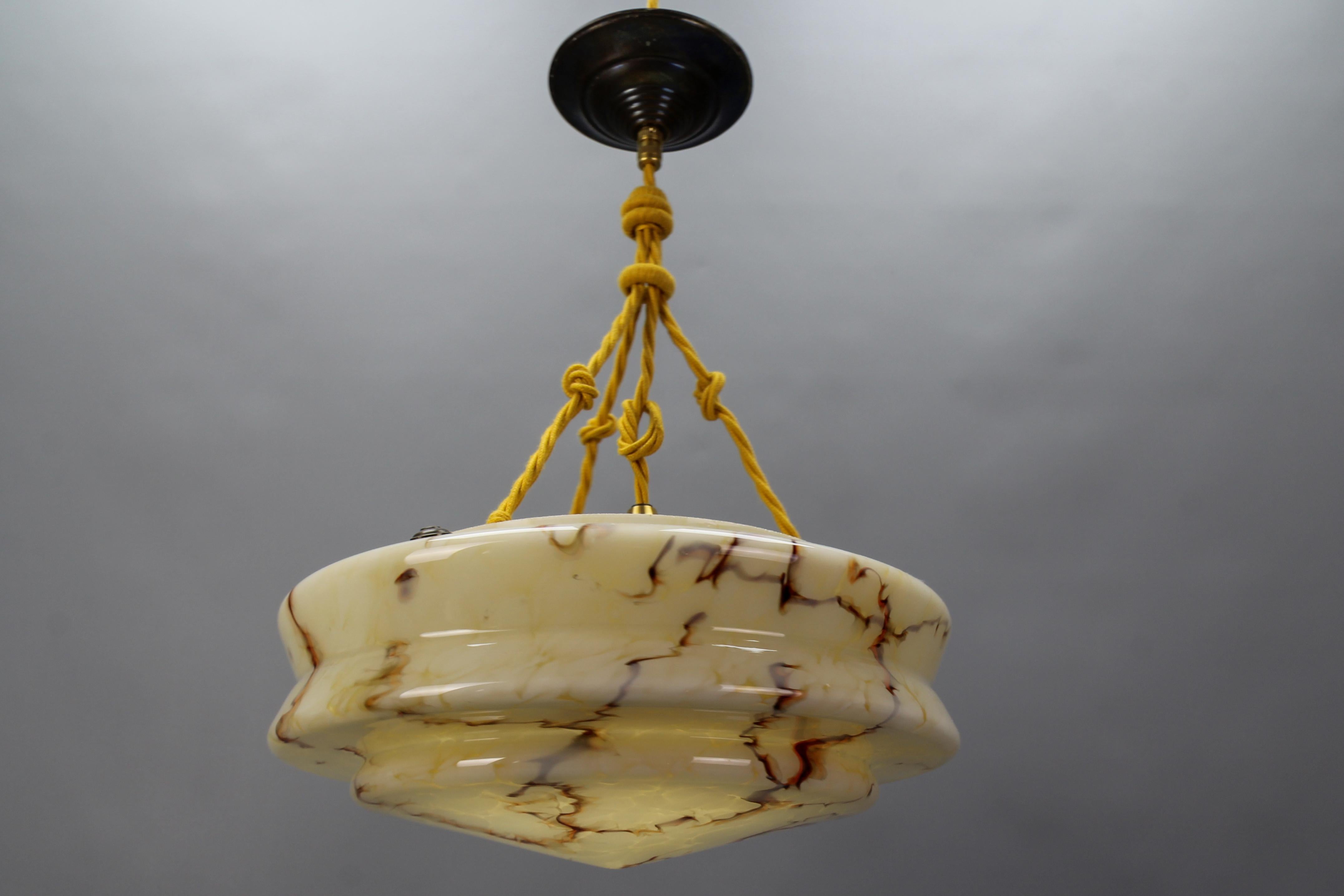 An Art Deco marbled amber color glass and brass pendant light from circa the 1930s, Germany.
This beautiful ceiling light fixture features a marbled glass lampshade - the shade blends a marbled dark yellow or amber color base with dark and light